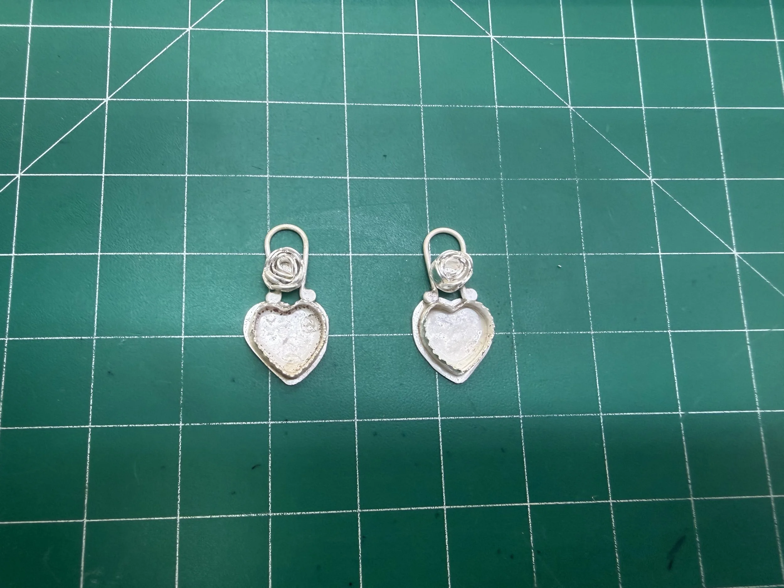 Unfinished sterling silver heart earrings with bezels on a work surface during a jewelry workshop in Albuquerque