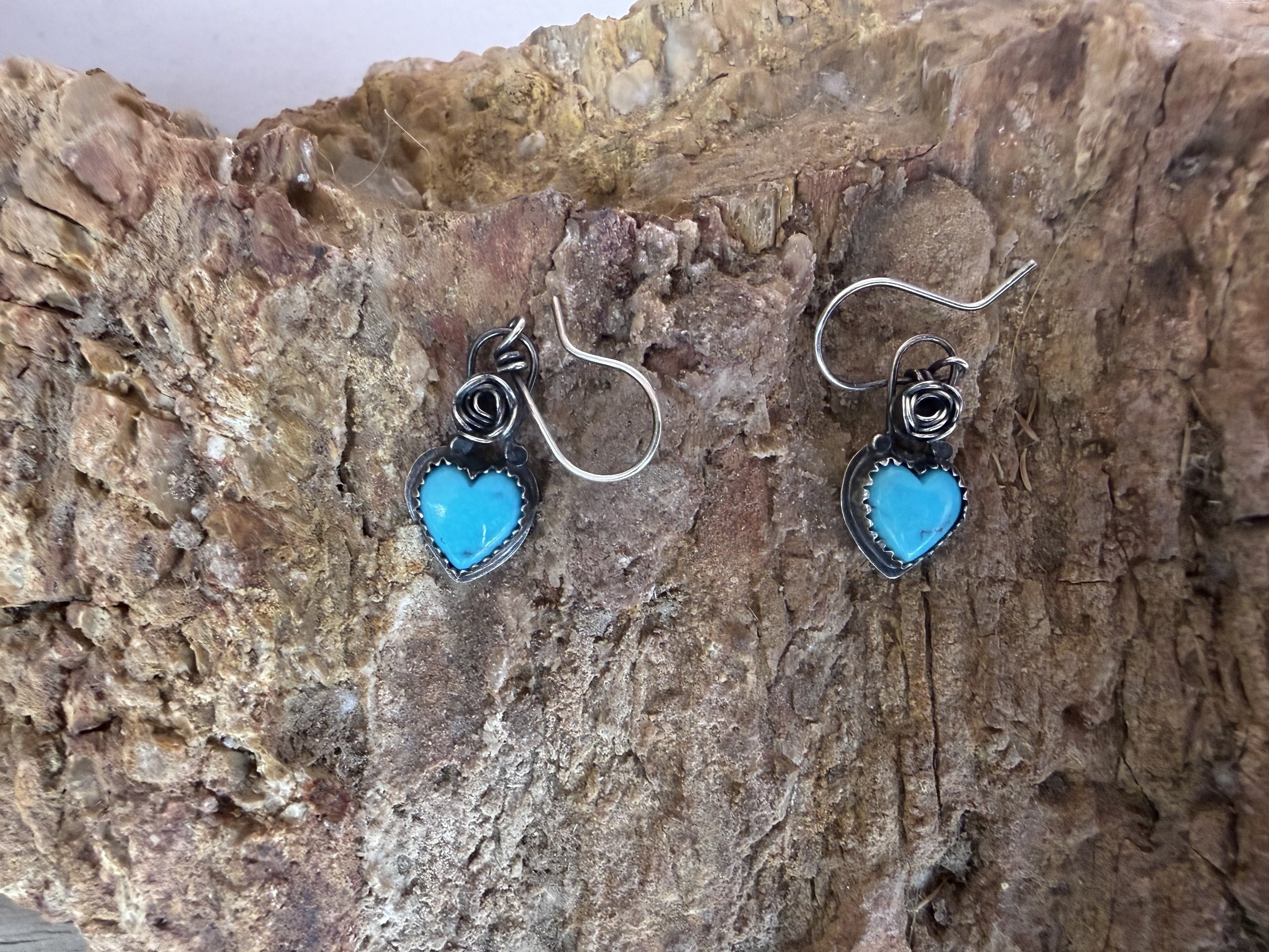 Turquoise heart earrings with silver rose detail displayed on stone after a jewelry workshop in Albuquerque