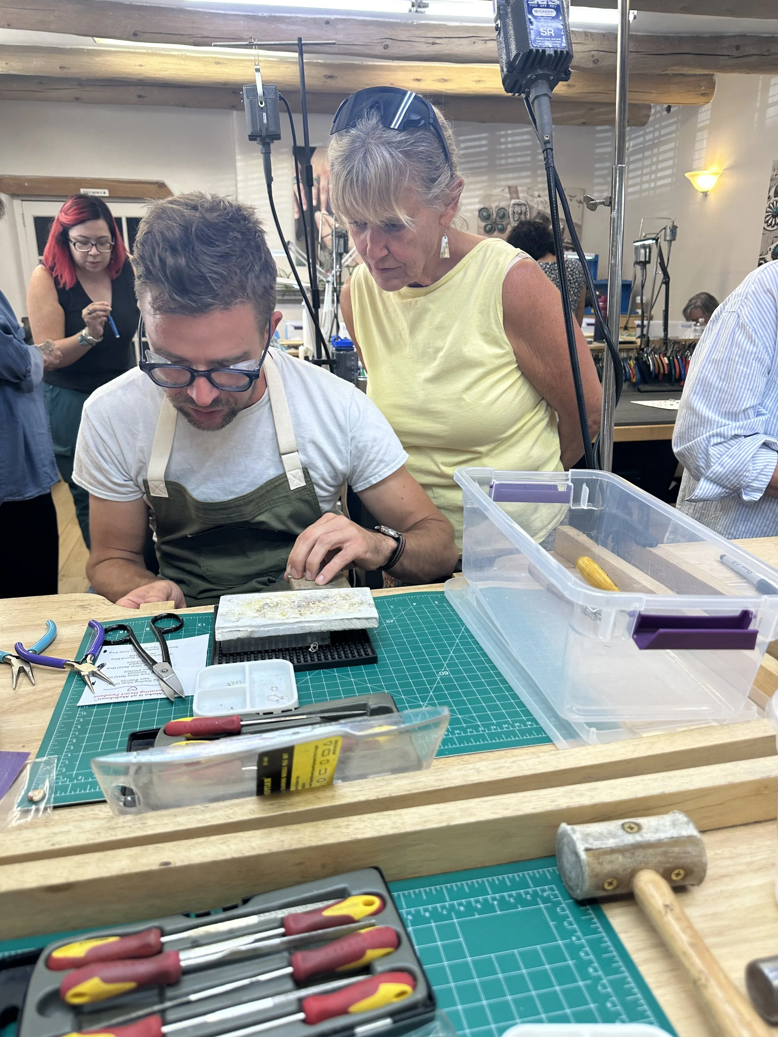 Instructor helping student shape pendant at bench, jewelry making class Albuquerque hands-on learning