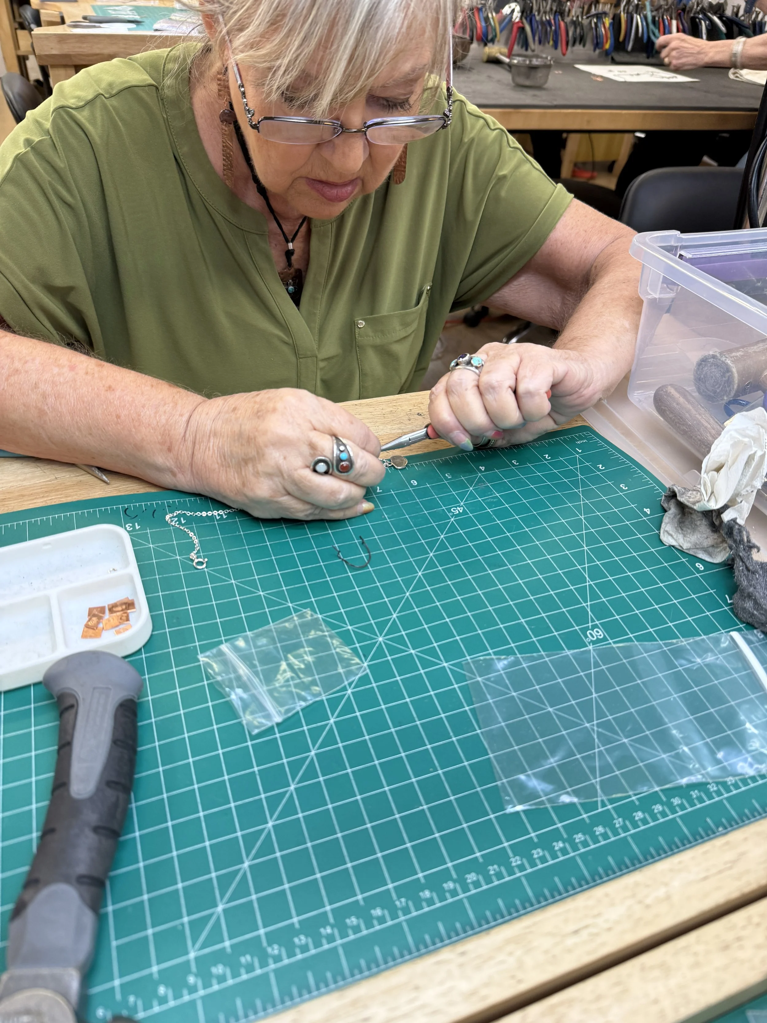 Jewelry making classes Albuquerque with a student shaping a silver charm.