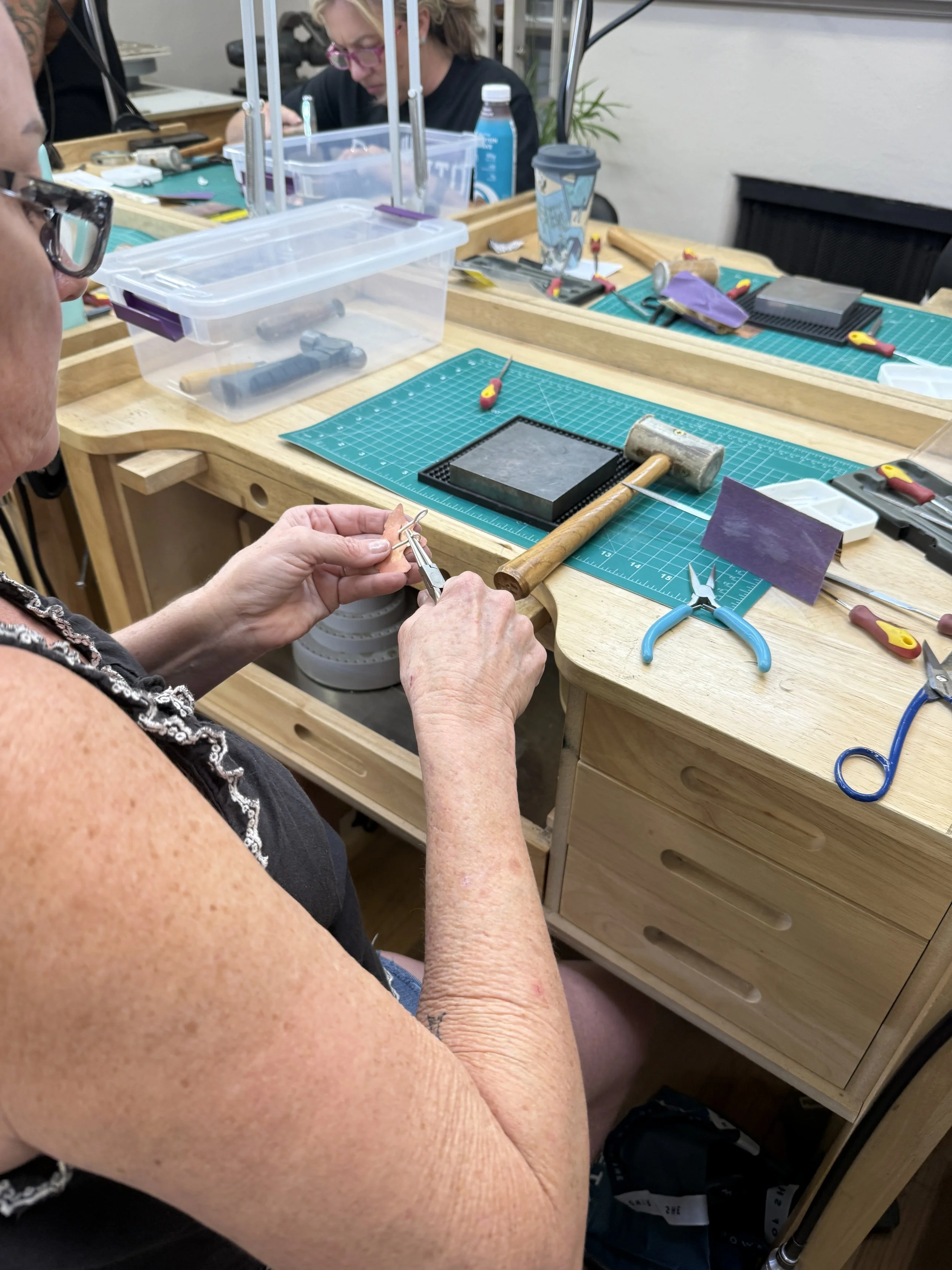 Student shaping a metal component with pliers during a jewelry-making class