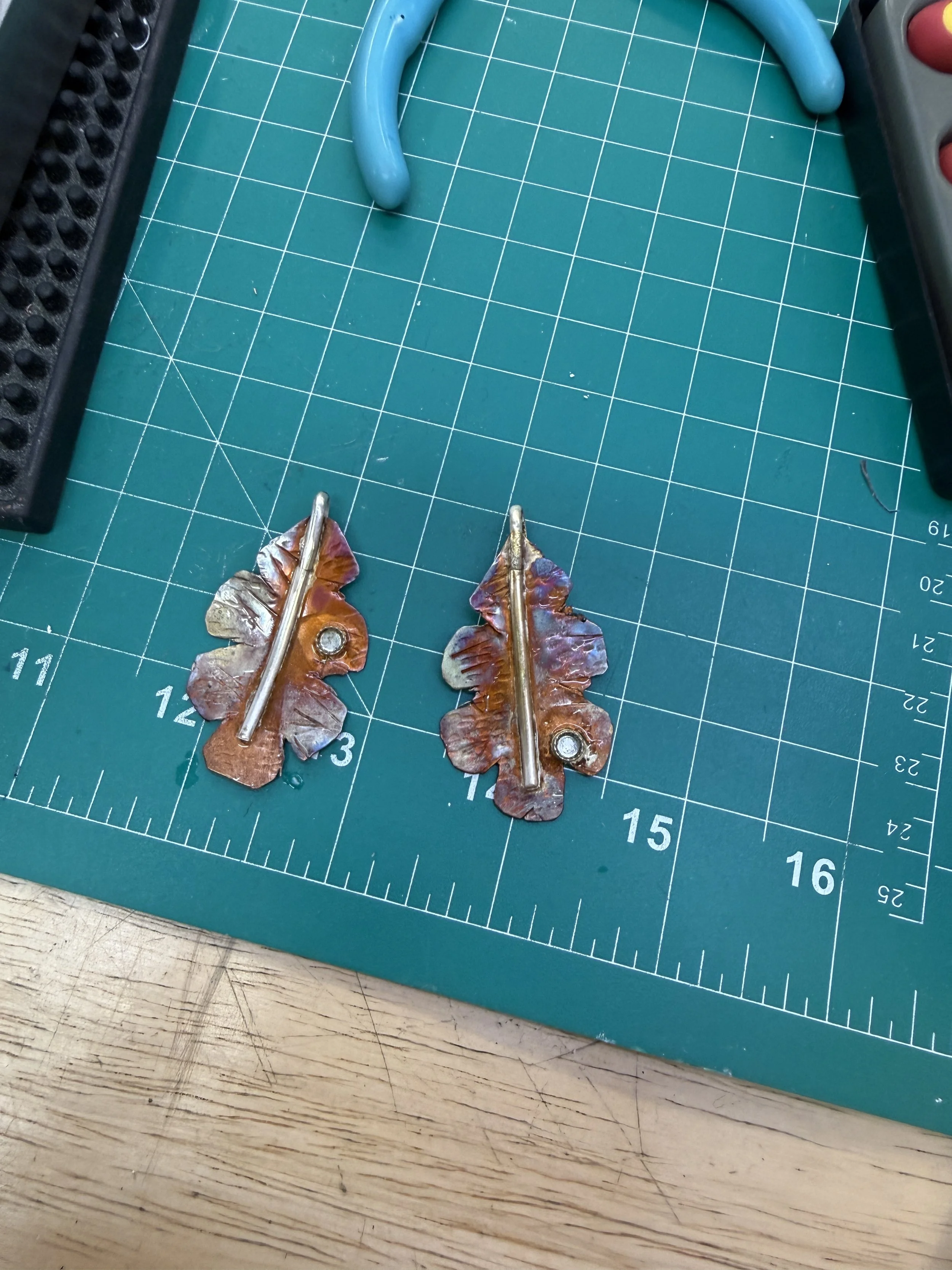 Finished copper leaf earrings with textured details and stone accents on a cutting mat