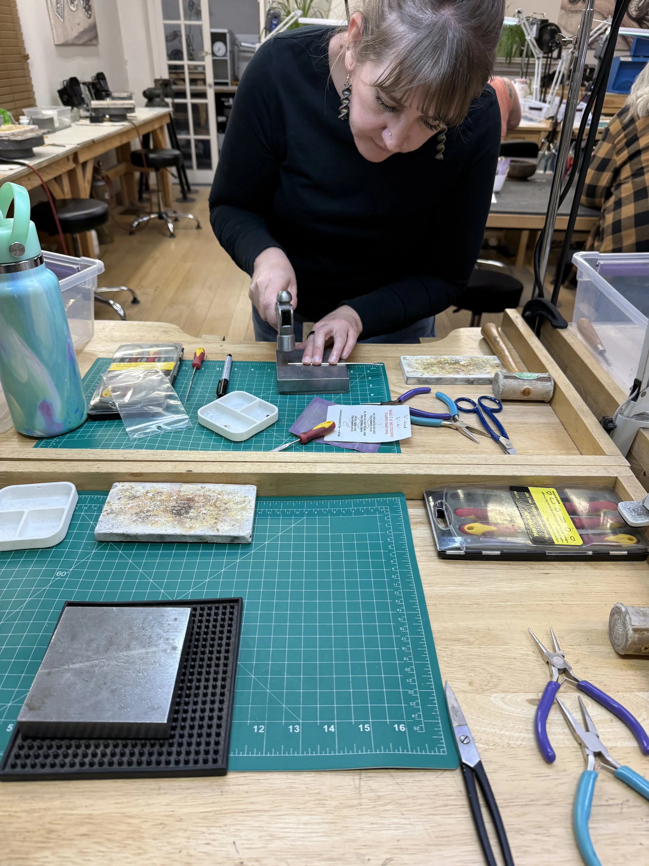 Student hammering a metal ring on a steel block at a jewelry workbench