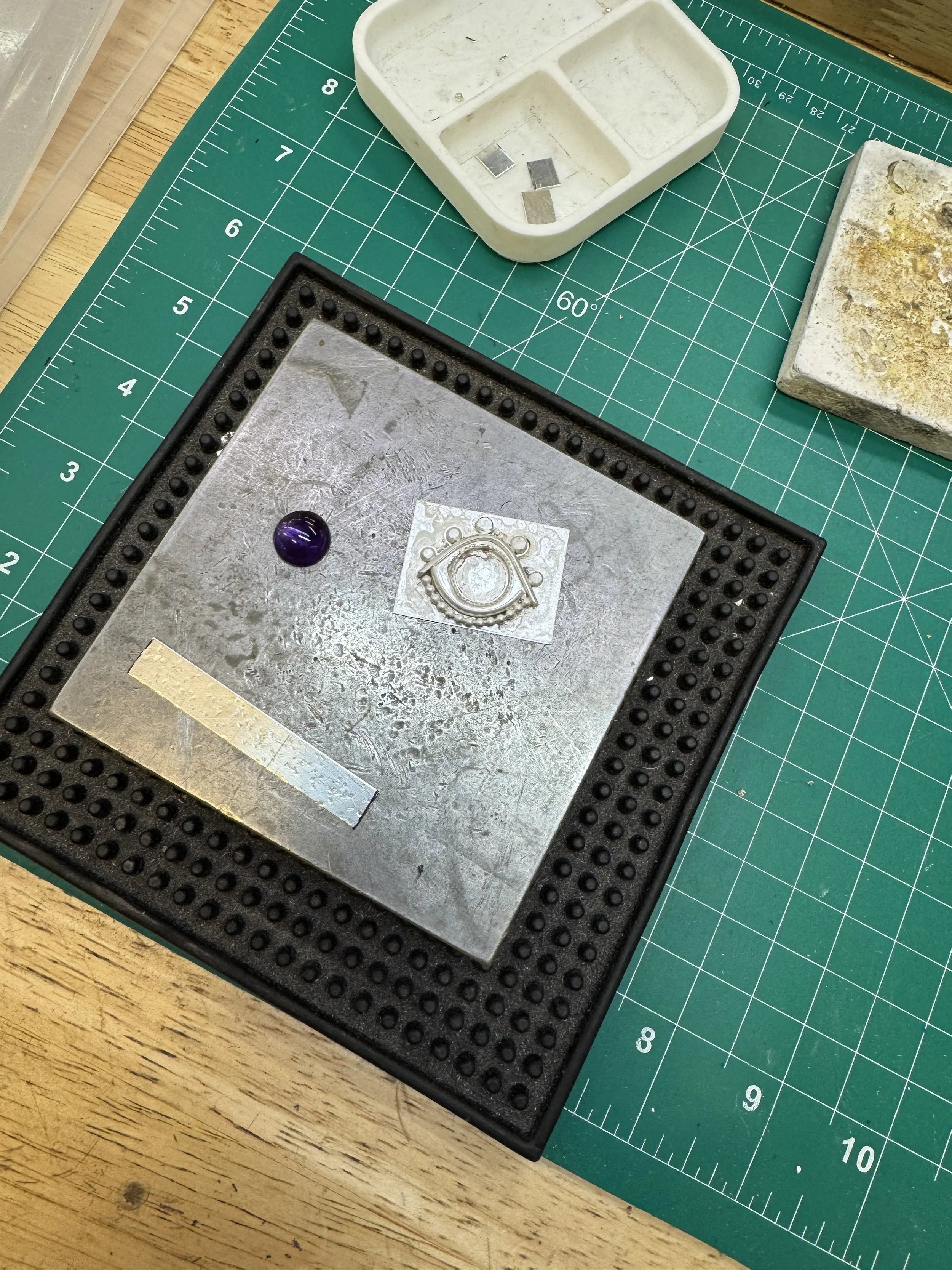 View of a silver ring setting in progress beside a cabochon stone