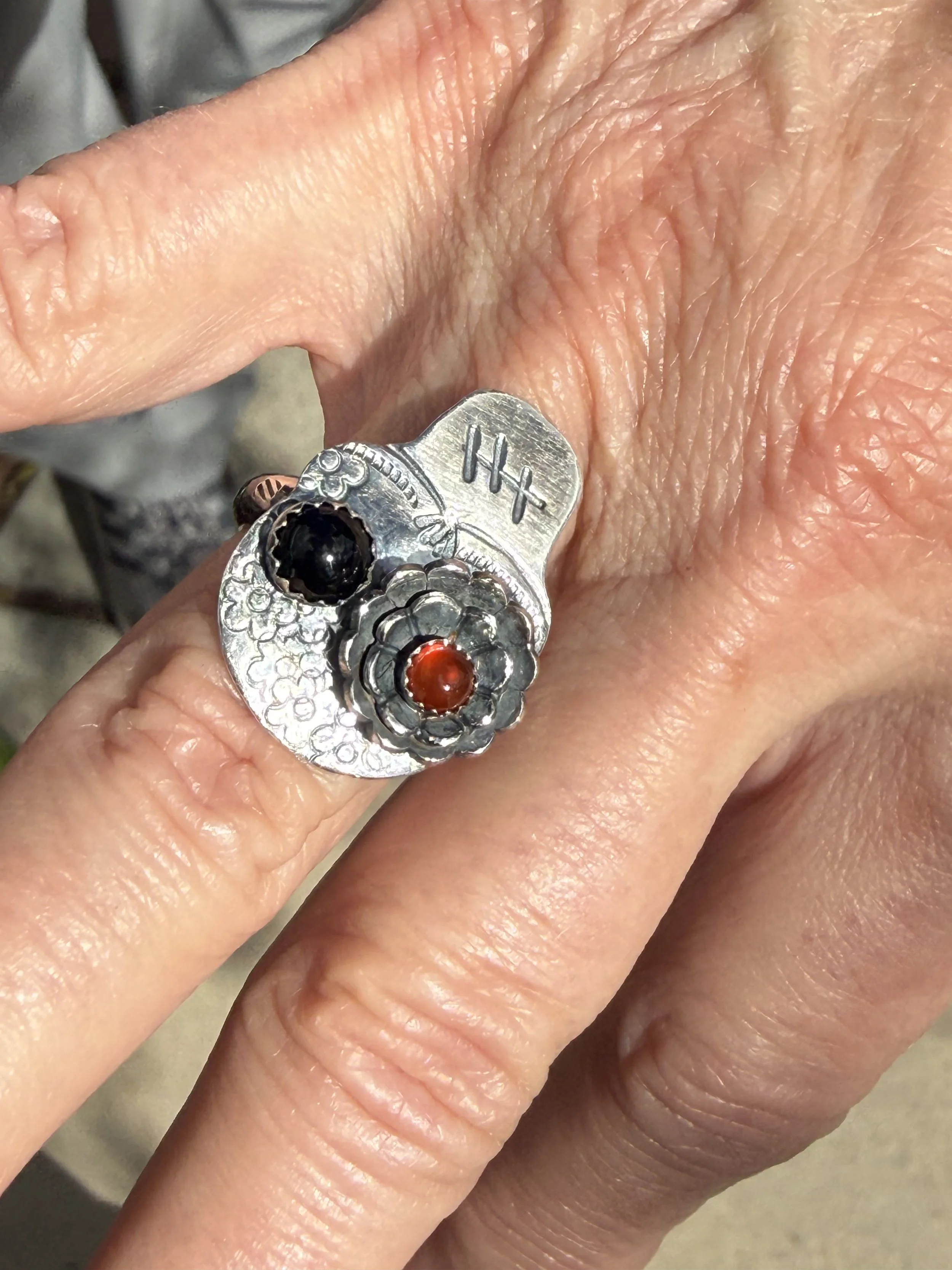 Close-up of a handcrafted silver skull ring with a red stone and floral accents