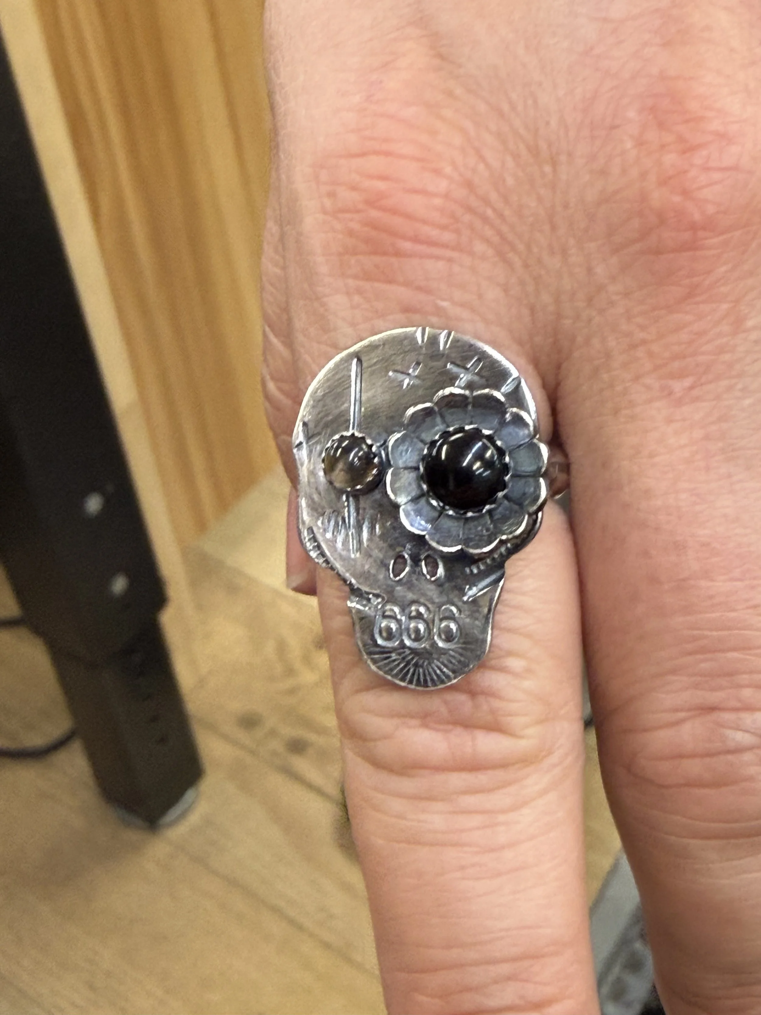 Handcrafted silver skull ring with a dark central stone and raised flower detail