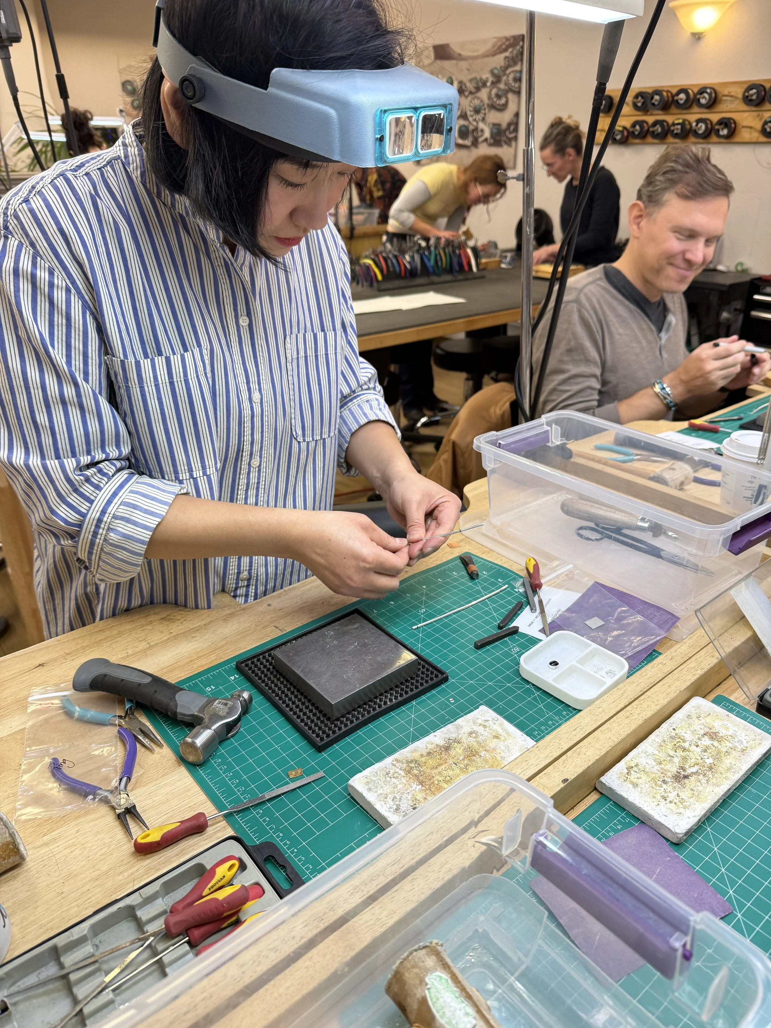 A student shaping a piece of silver at a jewelry-making workbench