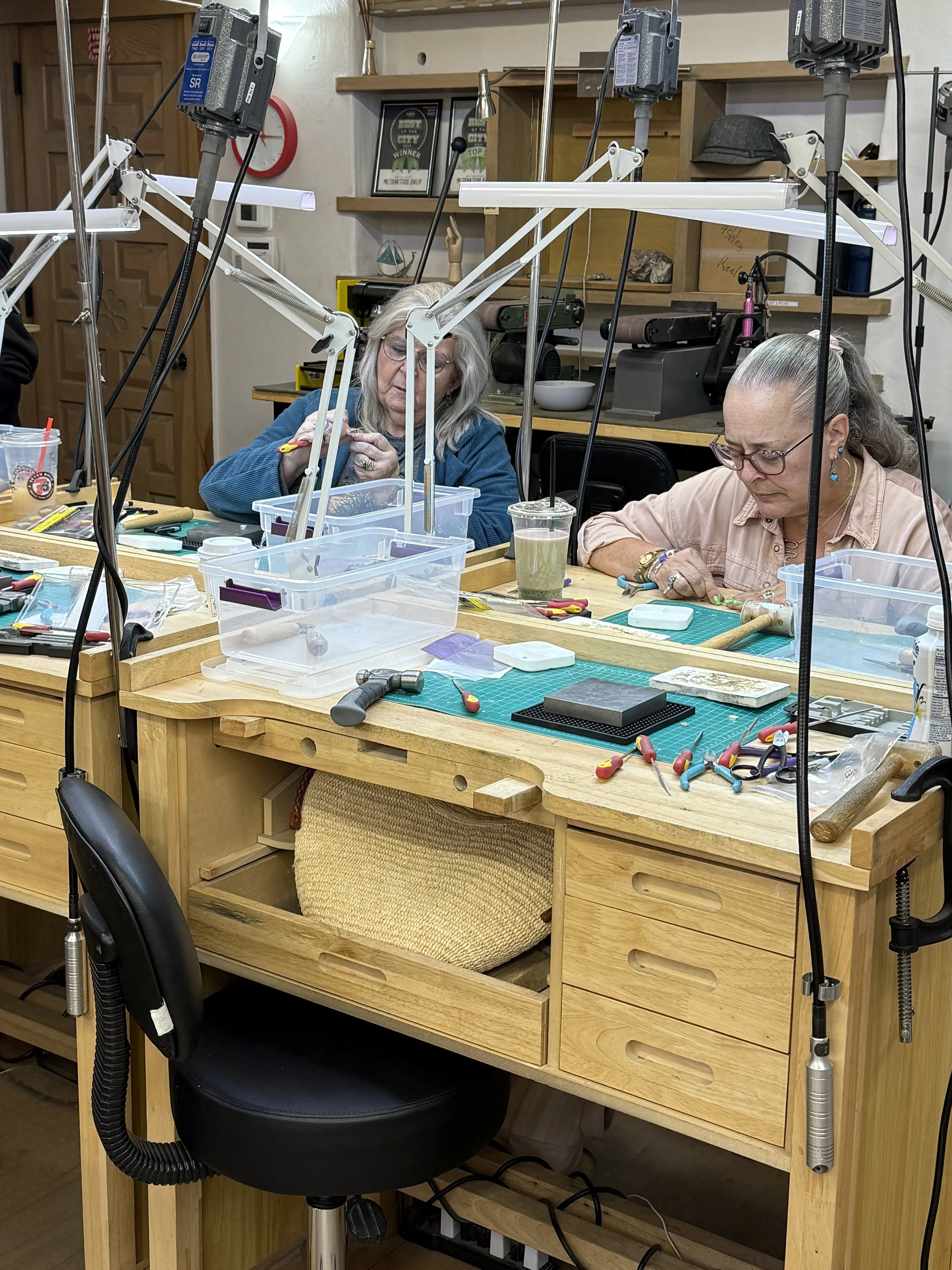Two students work on jewelry-making projects at their benches