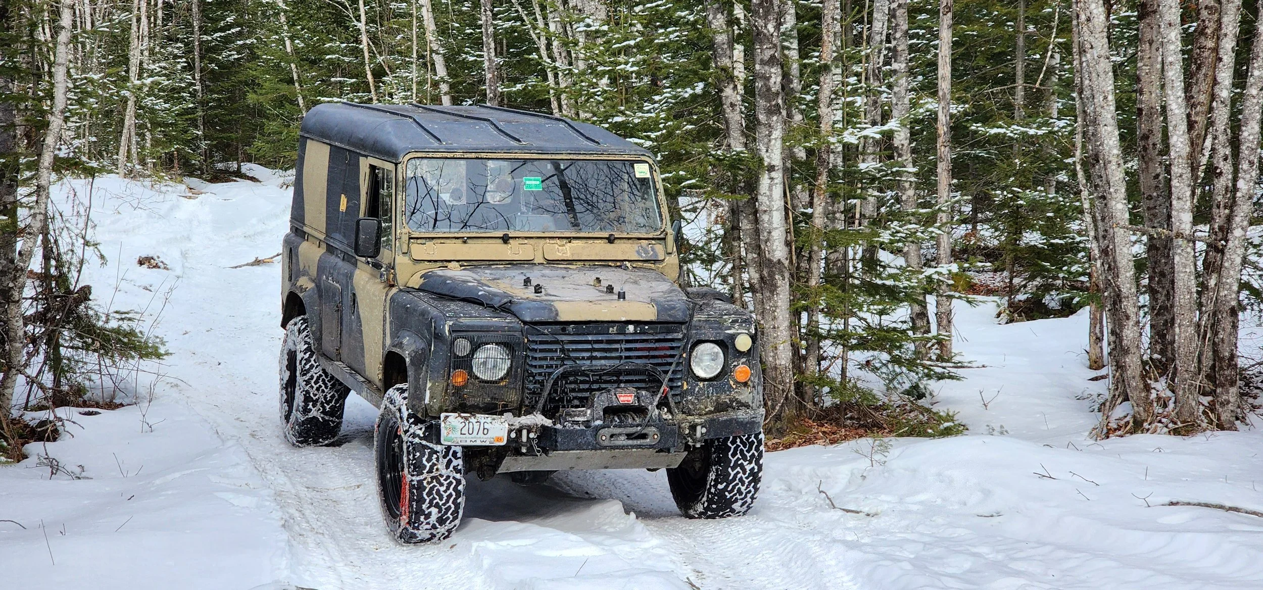 Defender 110 with snow chains on a winter trail in Maine