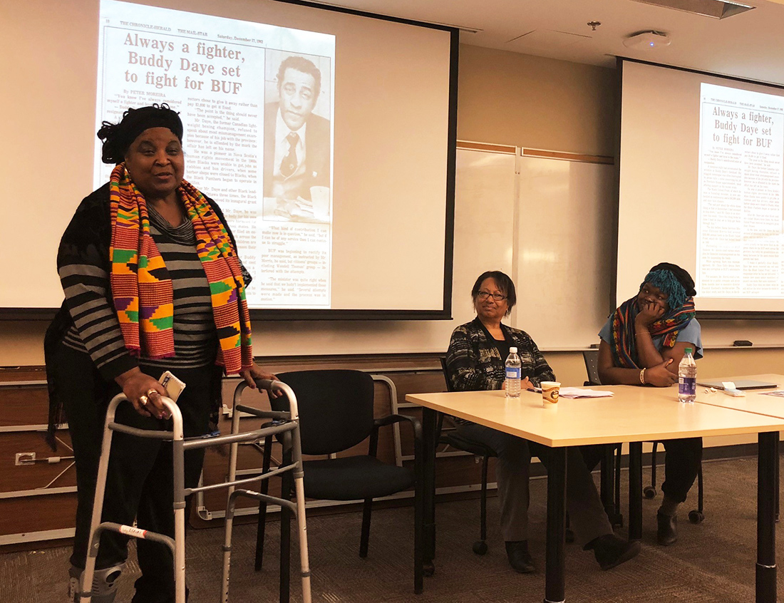 Dr. Lynn Jones addresses the audience as images from the Lynn Jones African-Canadian & Diaspora Heritage Collection appear in the slideshow behind her. The other panellists were Regina James (centre) of the East Preston Empowerment Academy, and researcher/filmmaker Francesca Ekwuyasi (at right).