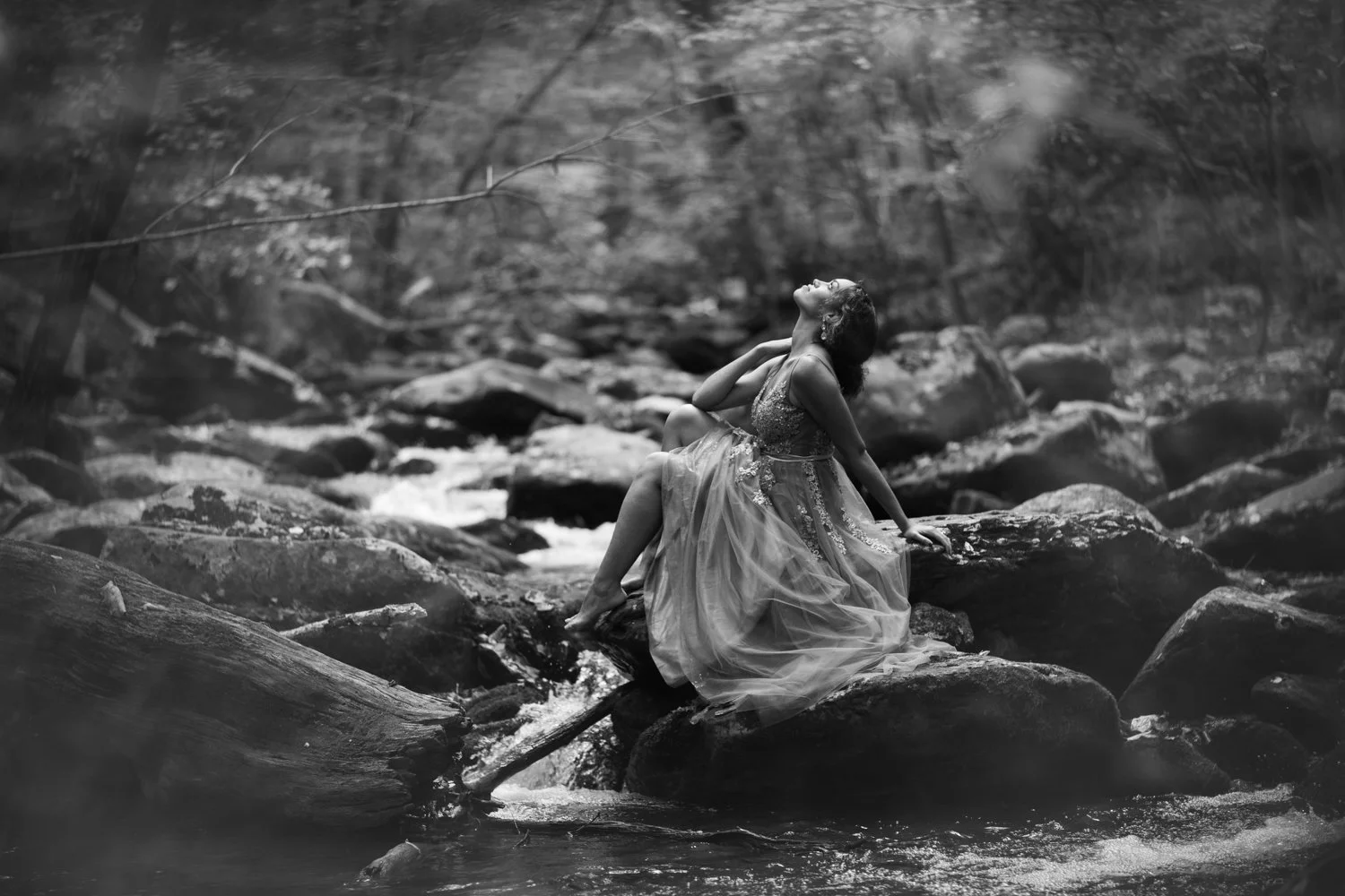 black and white boudoir portrait of a woman sitting on boulders in a river wearing a gown in the blue ridge mountains near Charlottesville, Virginia