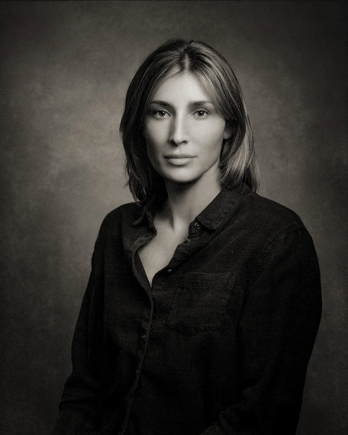 Black-and-white platinum-style studio portrait of a young woman with shoulder-length hair against a dark backdrop.