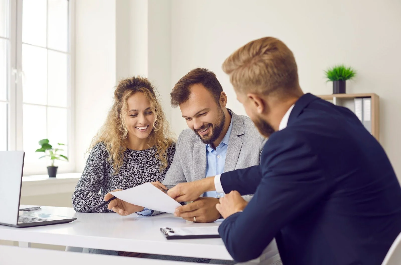 A business professional explains documents to a smiling couple in an office, building trust and nurturing a long-term client relationship.