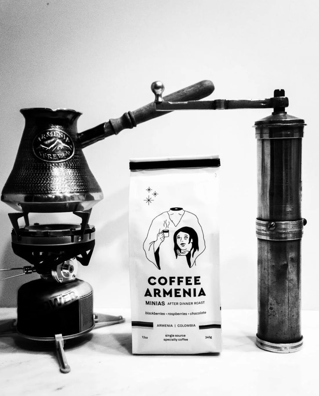 Hammered jezve stamped Armenia Yerevan on a small burner, a bag of Coffee Armenia Minias, and the Halebian family's century-old bronze Ottoman coffee grinder, in black and white