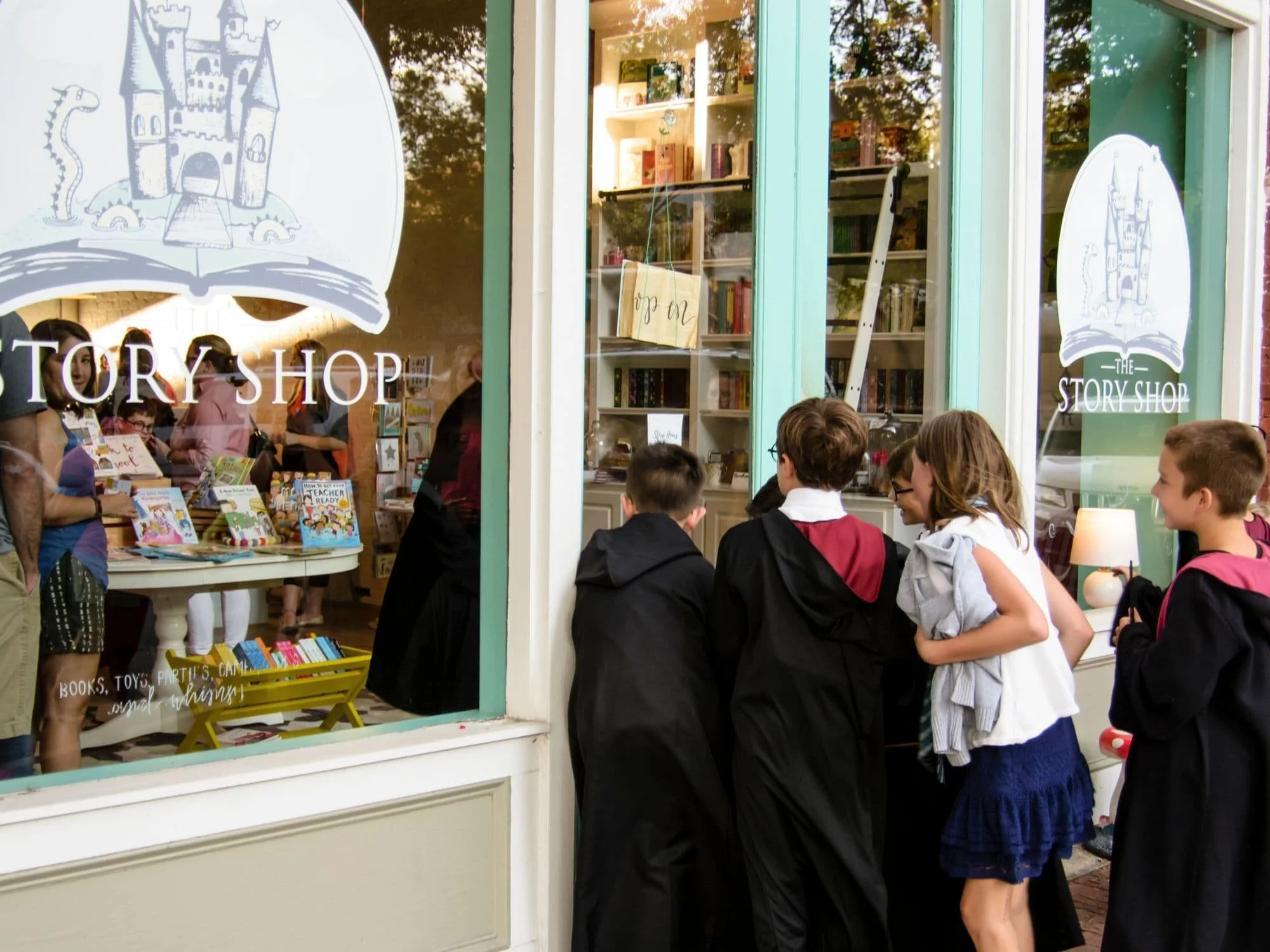 Children eagerly peeking through The Story Shop windows before stepping inside the whimsical children's bookstore in downtown Monroe, Georgia.
