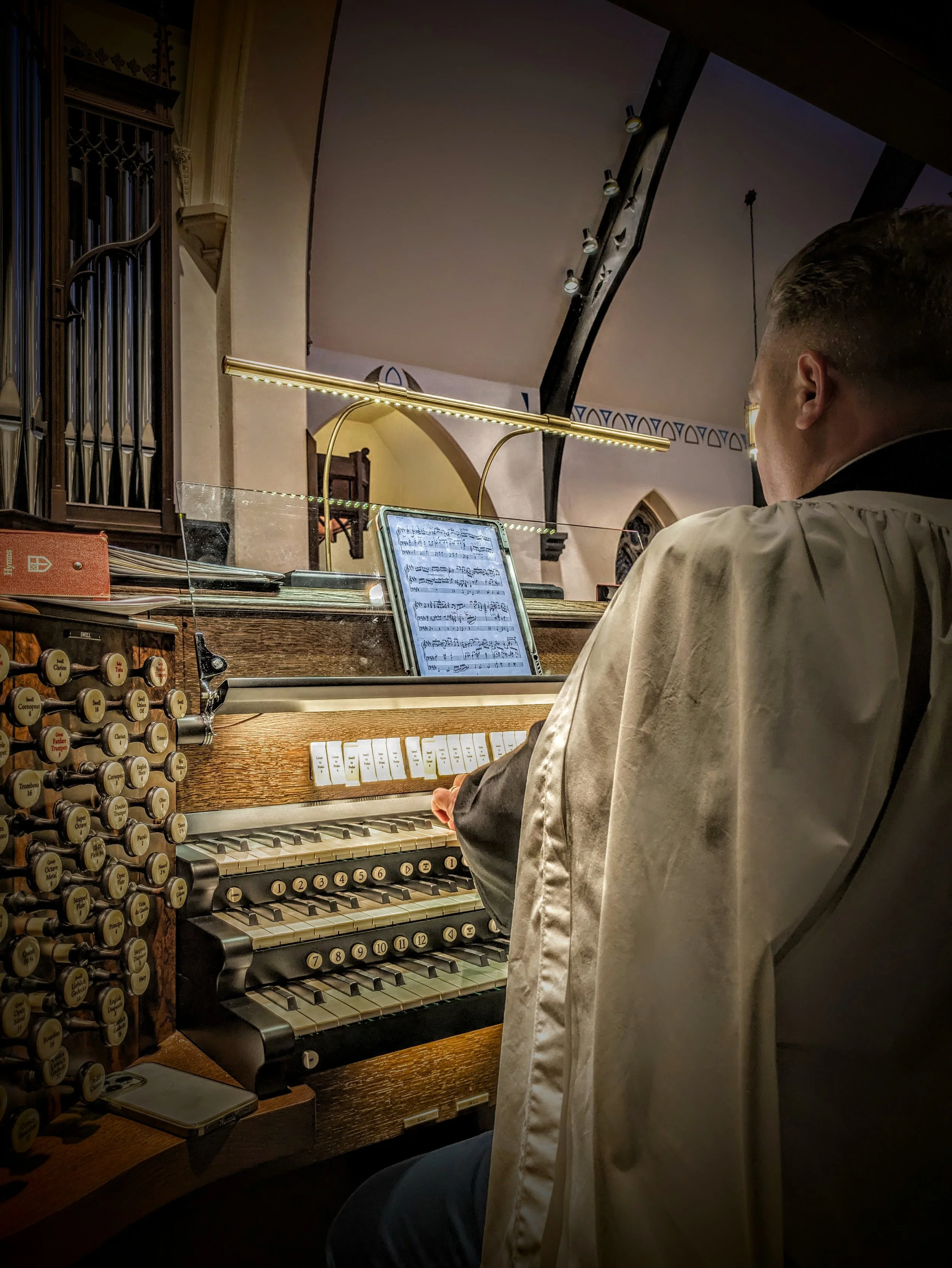 Organist playing the multi-manual pipe organ with illuminated sheet music during a service at Christ Church Glendale.