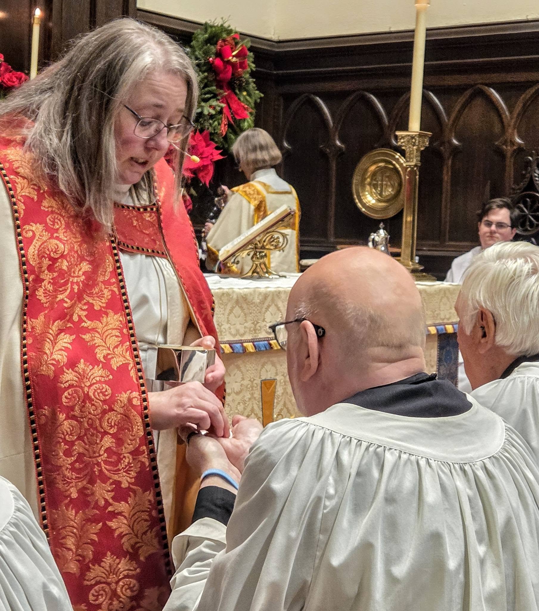 Clergy administering Holy Communion bread from a ciborium to choir members at the altar during a festival service at Christ Church Glendale.