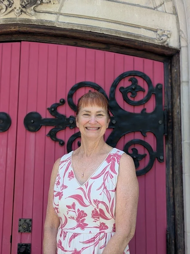 Portrait of Karen Corbett, Parish Administrator at Christ Church Glendale standing in front of a red door at CCG
