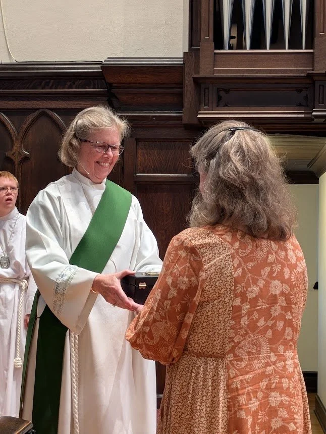 Deacon Anne Reed handing a Eucharistic visitor kit to a lay minister before the altar at Christ Church Glendale, Ohio.