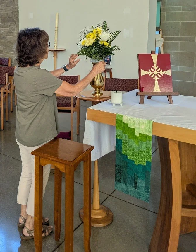 A member of the Christ Church Glendale Altar Guild arranges yellow and white altar flowers on a brass stand in the sanctuary.