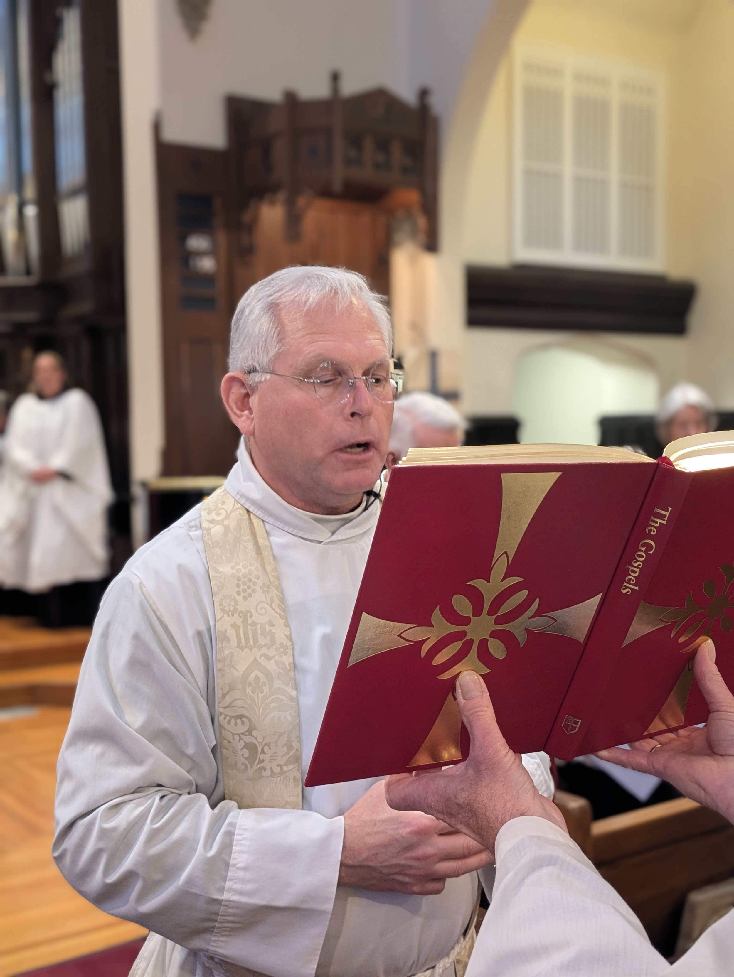 Father David Pfaff proclaiming the Holy Gospel from the red Gospel Book during Sunday Eucharist at Christ Church Glendale, Ohio.