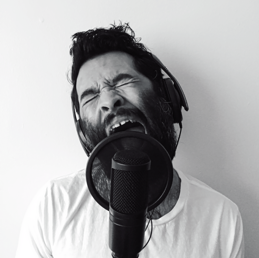 스튜디오 녹음 마이크에 대고 노래를 부르는 흑백 흉상 사진으로 한 남자가 헤드폰을 쓰고 하얀 티셔츠를 입고 있습니다. 입을 벌리고 눈을 꼭 감고 표정 있는 순간 고개를 갸웃거립니다.