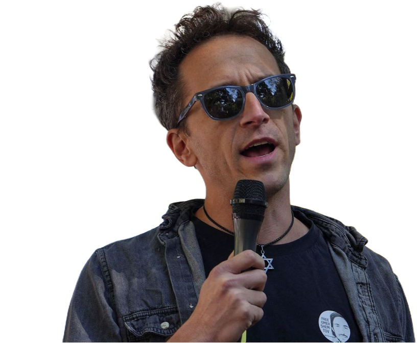 Man with sunglasses speaking into a microphone, wearing a black shirt with a button and a star of David necklace.