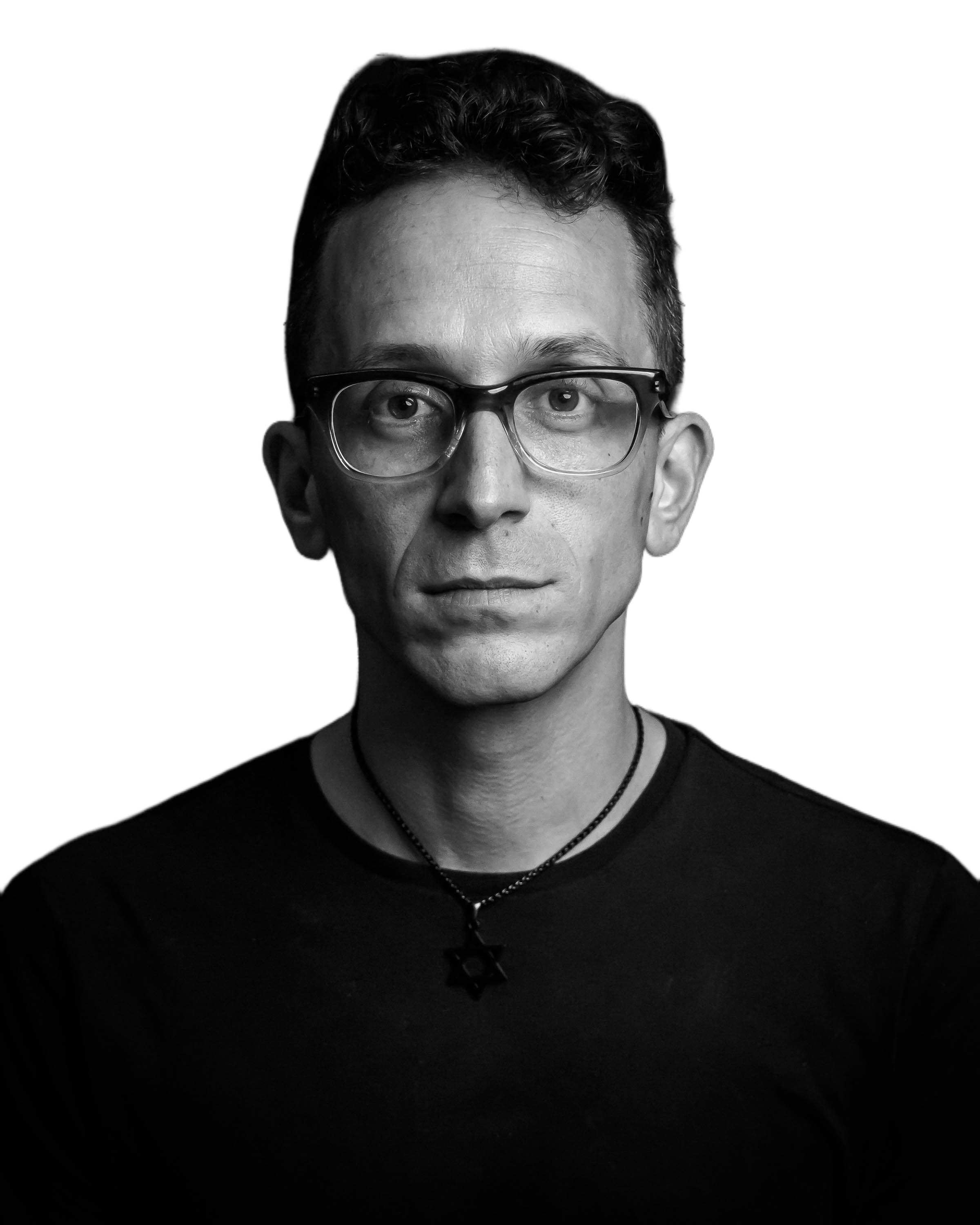 Black and white portrait of a man with curly hair, glasses, and a Star of David necklace against a black background.