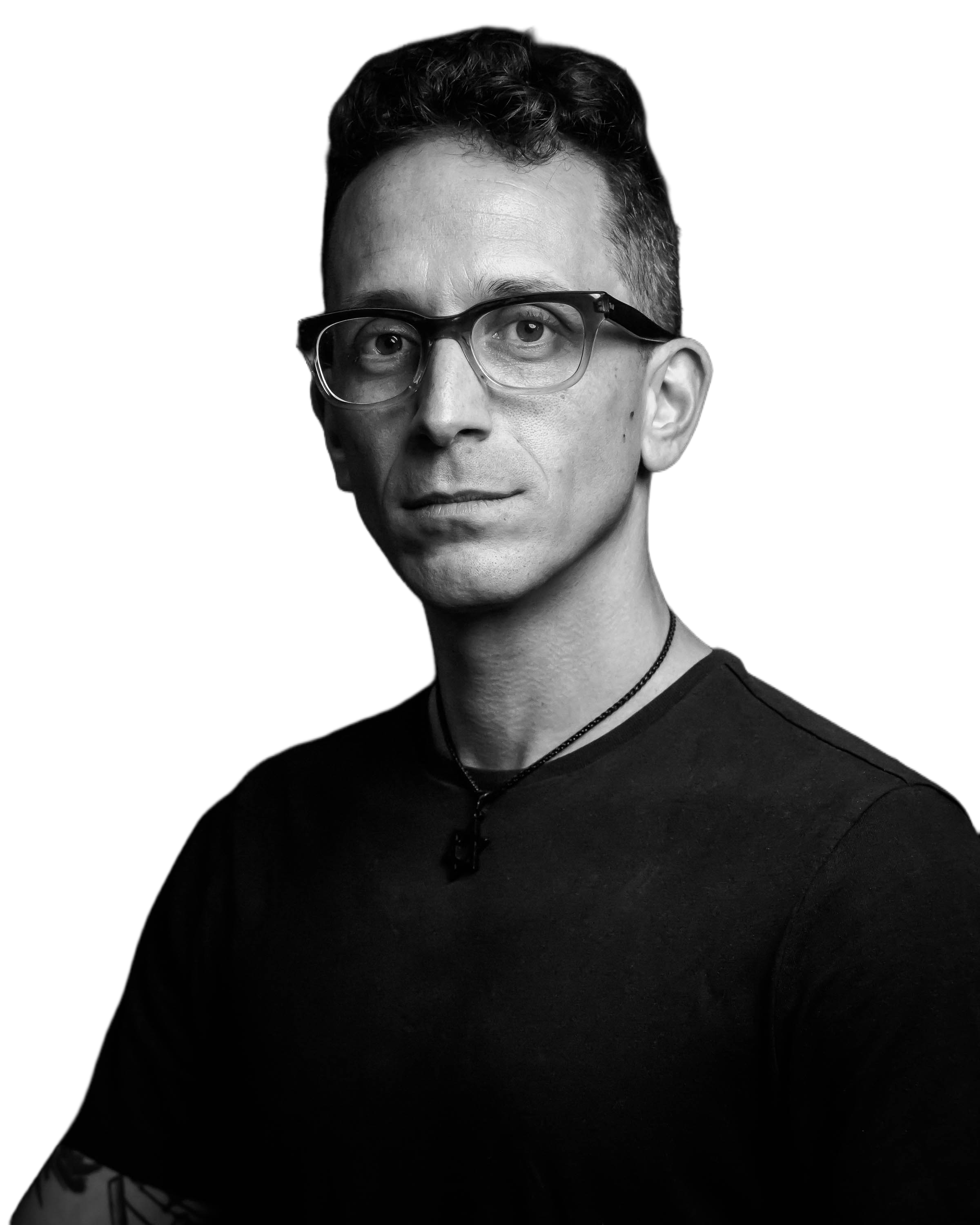 Black and white portrait of a person wearing glasses and a necklace, against a dark background.