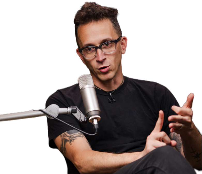 A man with glasses and tattoos speaking into a microphone during a recording or podcast session.