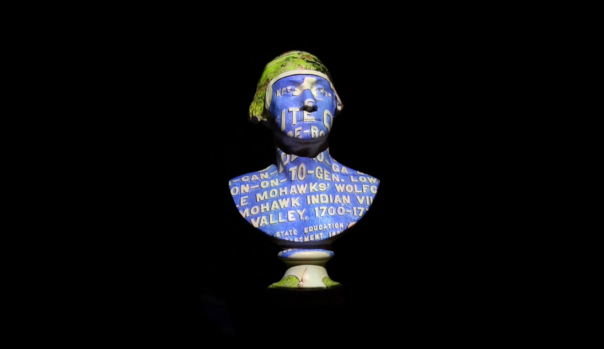 An installation of video projected onto a bust of George Washington mounted on a surveyor’s tripod. During the Revolutionary War, Washington, known to the Haudenosaunee (Six Nations) as Hanödaga:yas, or Town Destroyer, ordered a brutal campaign against them in which his generals devastated some 60 villages, and hundreds of prosperous houses, farms, and orchards. Seizing livestock and goods, his armies burned the rest to the ground, destroying the food supply and forcing the people to flee as refugees to Niagara, to starve through a frigid, lean winter in which many died. Through historic maps, documents, portraits, site markers and other materials, the video traces the course of the campaign and the seizure of Haudenosaunee homelands in its aftermath. The artist is grateful to the Woodland Cultural Centre and members of Six Nations for their generous contributions to the sound track.