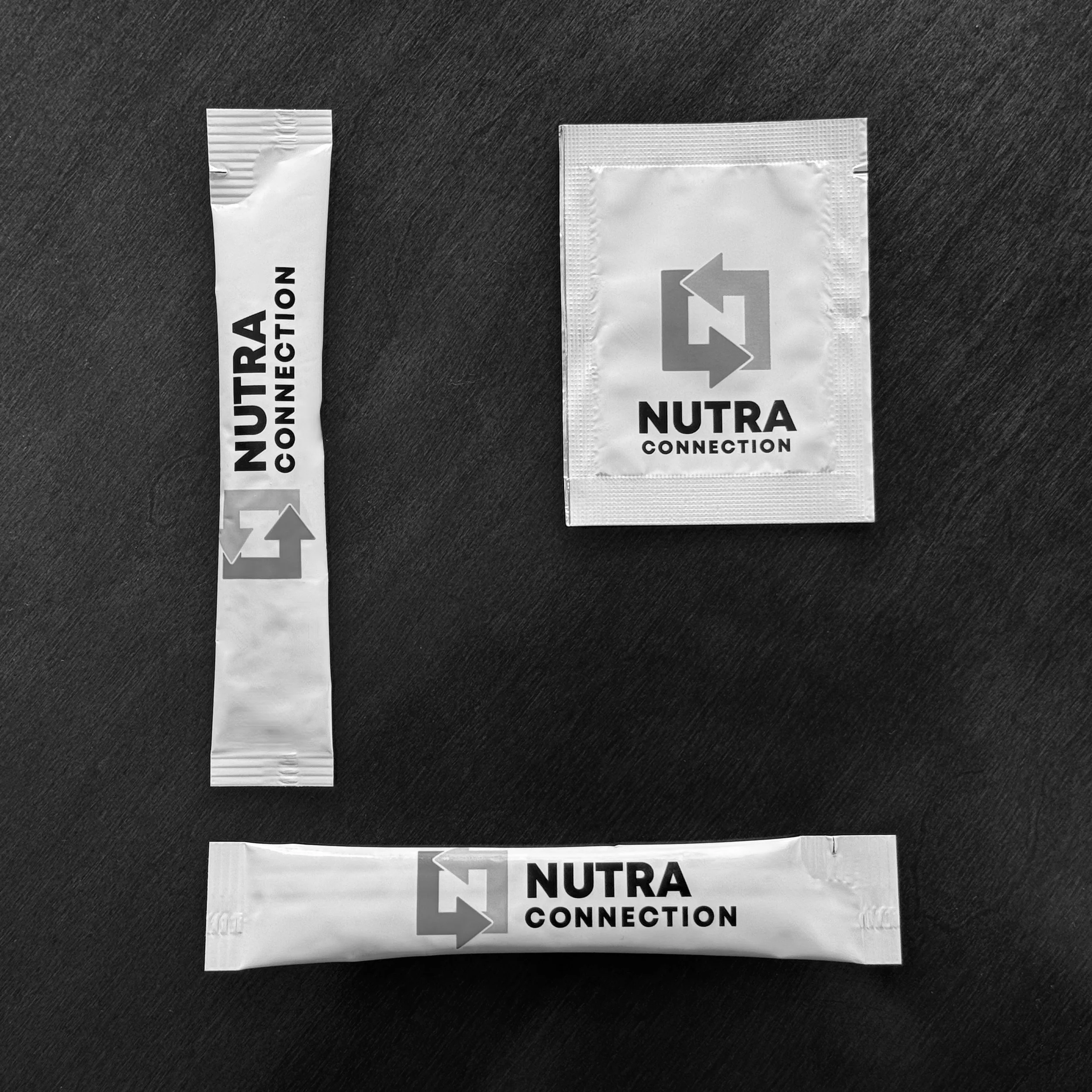 Image of two stick packs and one sachet next to each other on a dark background.