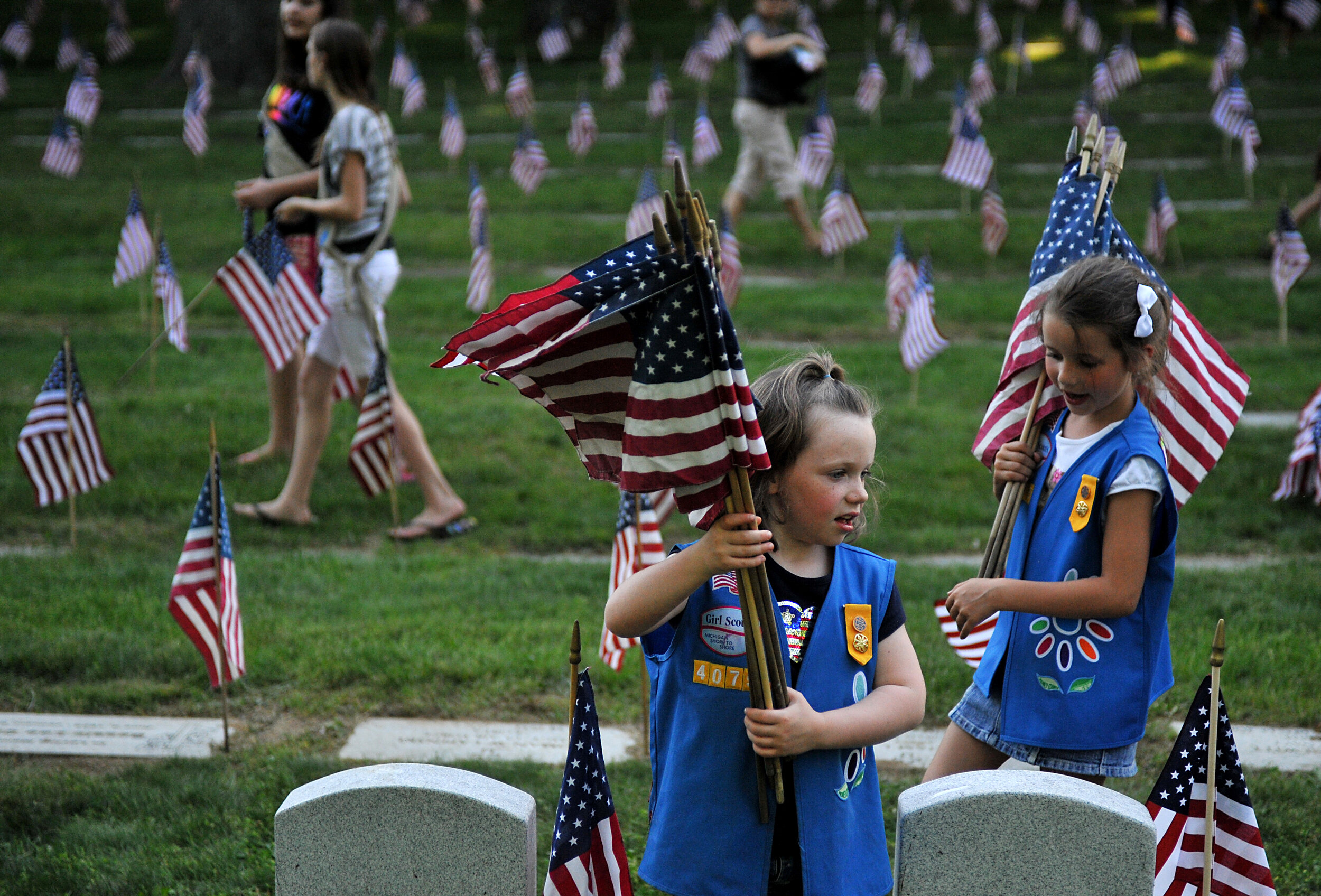  Natalie Benson, 5, and Holly Sweezer, 6, carry extra flags as Boy and Girl Scouts place flags on each of the 5,000 headstones at the Grand Rapids Veterans State Cemetery Wednesday, May 23, in Grand Rapids. 