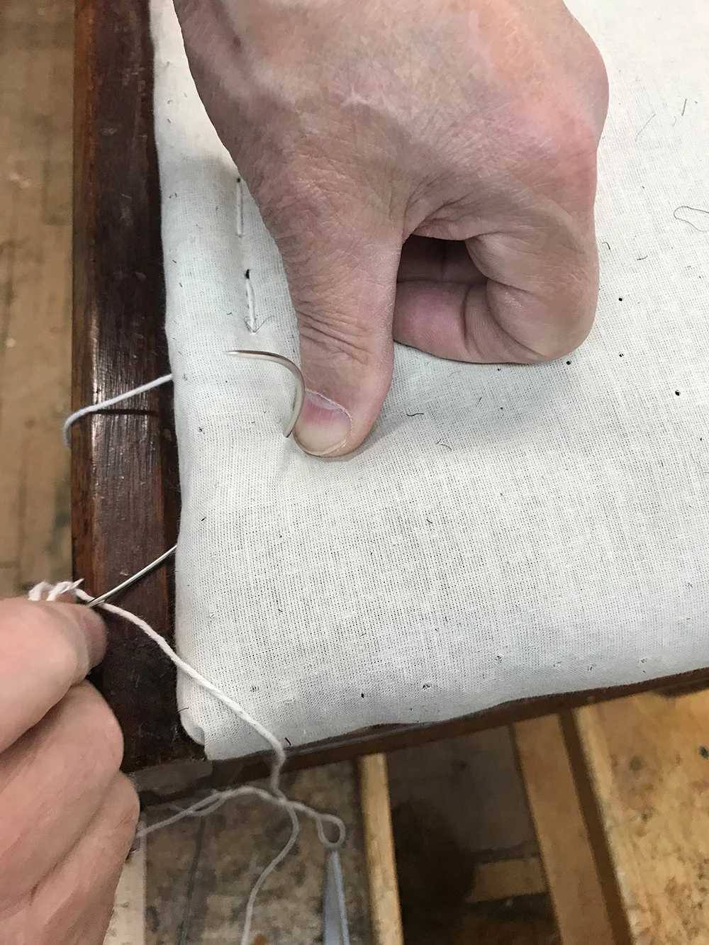 Curved round point needle penetrates muslin covered horse hair padding to create an edge roll.