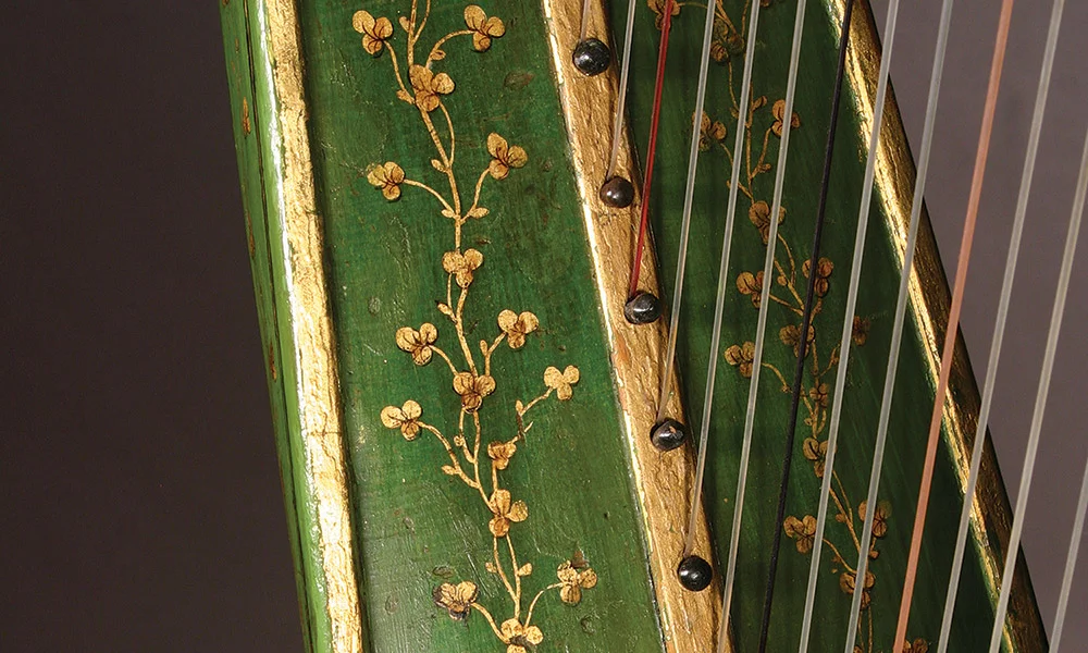 ... The harp is elaborately decorated with oil gilt 23.5 karat gold leaf highlights. The molding of the neck and the center and side strips of the soundboard are covered. There are gilt shamrocks everywhere, on all of the sections. These are surrounded by gilt lines and culminate in areas of scrolled foliage and abstract decorative elements. The gilding is defined and detailed with black lines. There were many areas of previous repairs to the gilding and black line work but the overwhelming majority of the decoration was original. The gilding repairs were the typical mix of various binders – mainly shellacs and nitro-cellulose lacquers, and various pigments – a mix of mostly copper alloy powders in various stages of oxidation and some areas of possible gold or mica powders. The touch-ups were the typical lower skill level than the original and often covered or confused existing original elements. Over all the harp’s finish was stable, bit dirty and in need of a cleaning of dust and grime. Read full story...