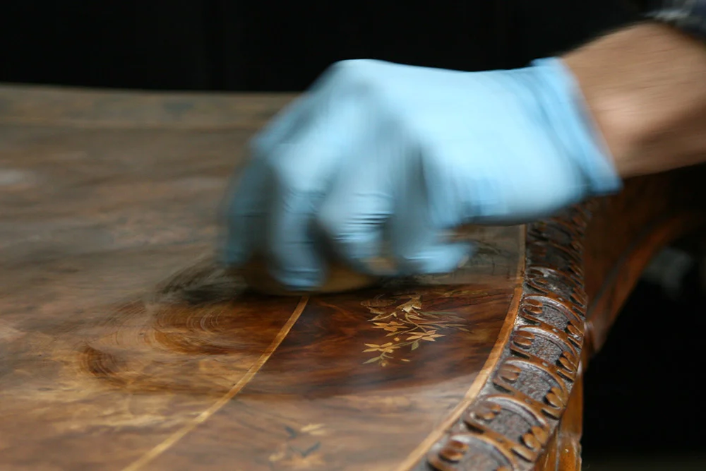 The first layer of French polish is applied to the restored table surface. Soon, shellac will immediately highlight marquetry patterns and wood grain