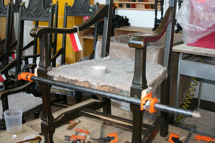 Clamping the wood frames after insertion of glue to re-stabilize the joints which loosened due to expansion and shrinkage cased by moisture exposure
