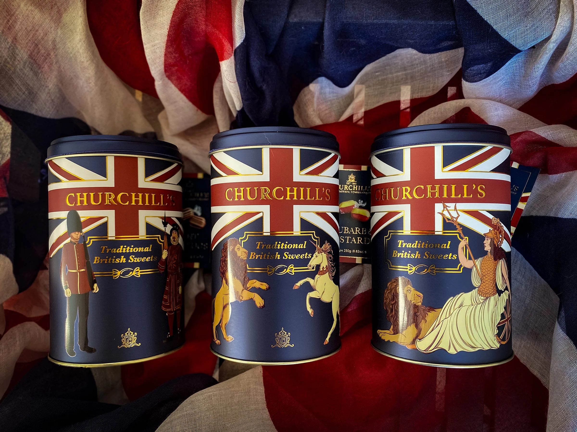 Three cylindrical tins of Churchill's sweets decorated with the Union Jack flag and traditional British figures.