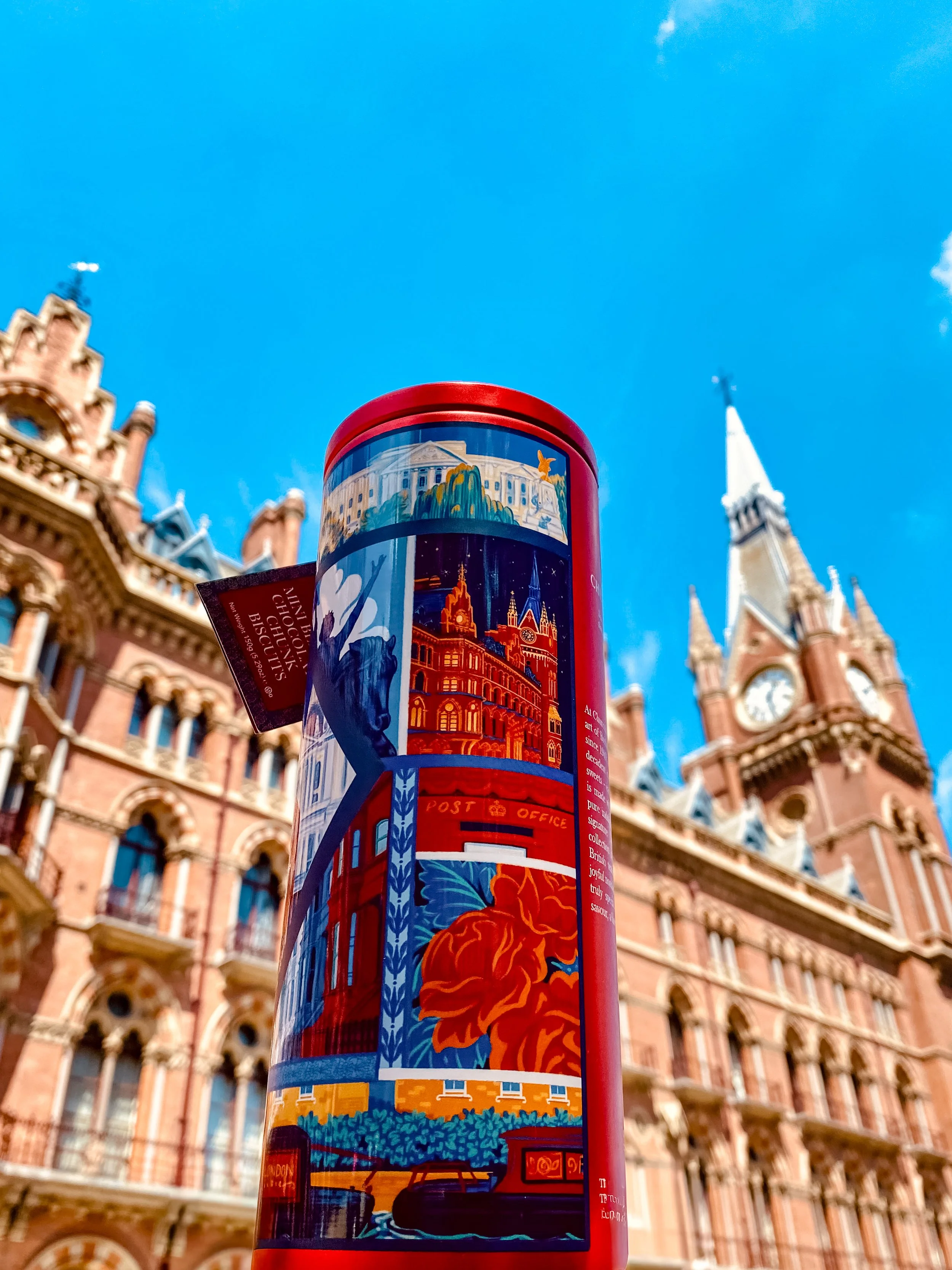 Red cylindrical tin with illustrated London landmarks against a red brick building and blue sky.