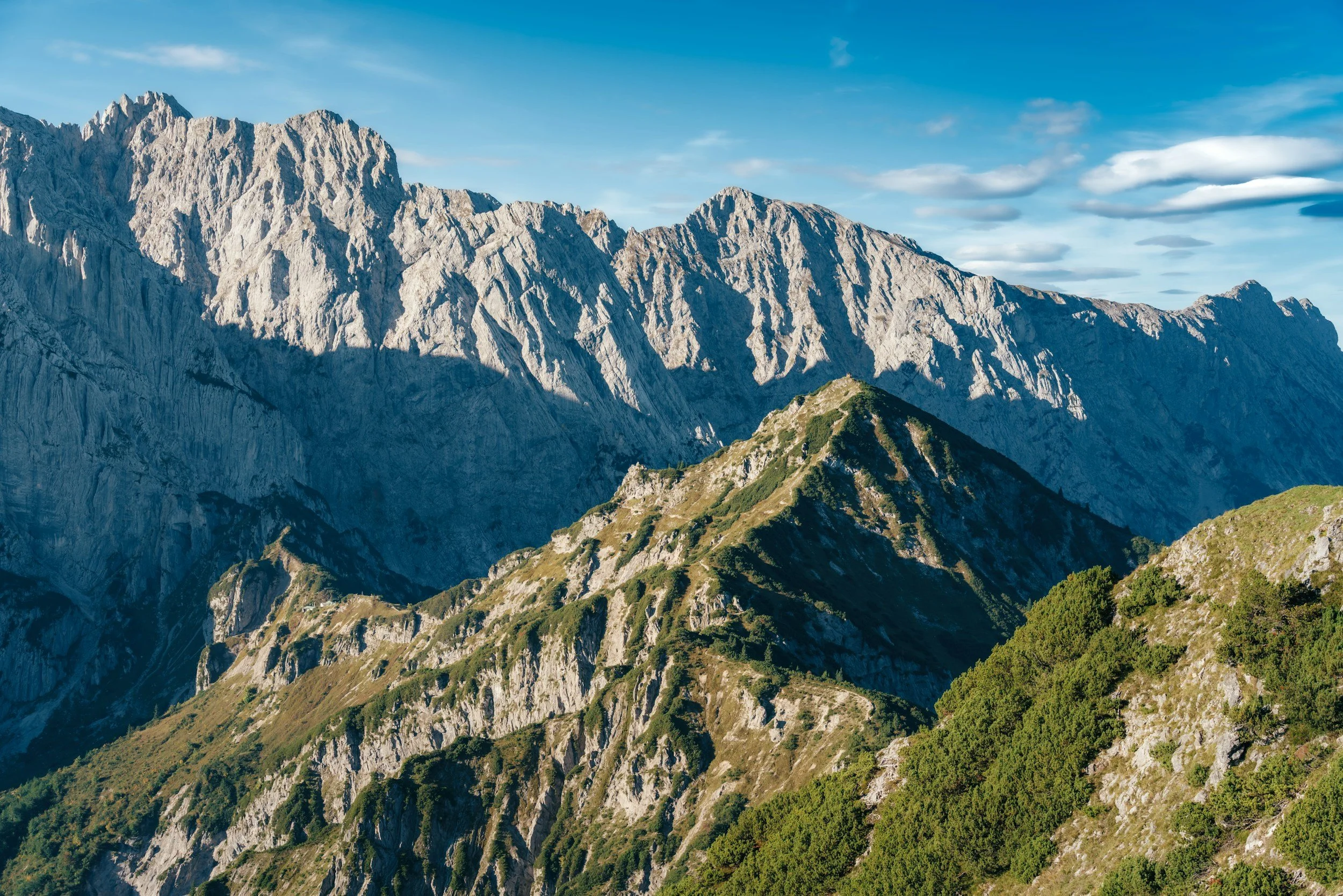 Mountain range with rocky peaks and green slopes under a partly cloudy sky.