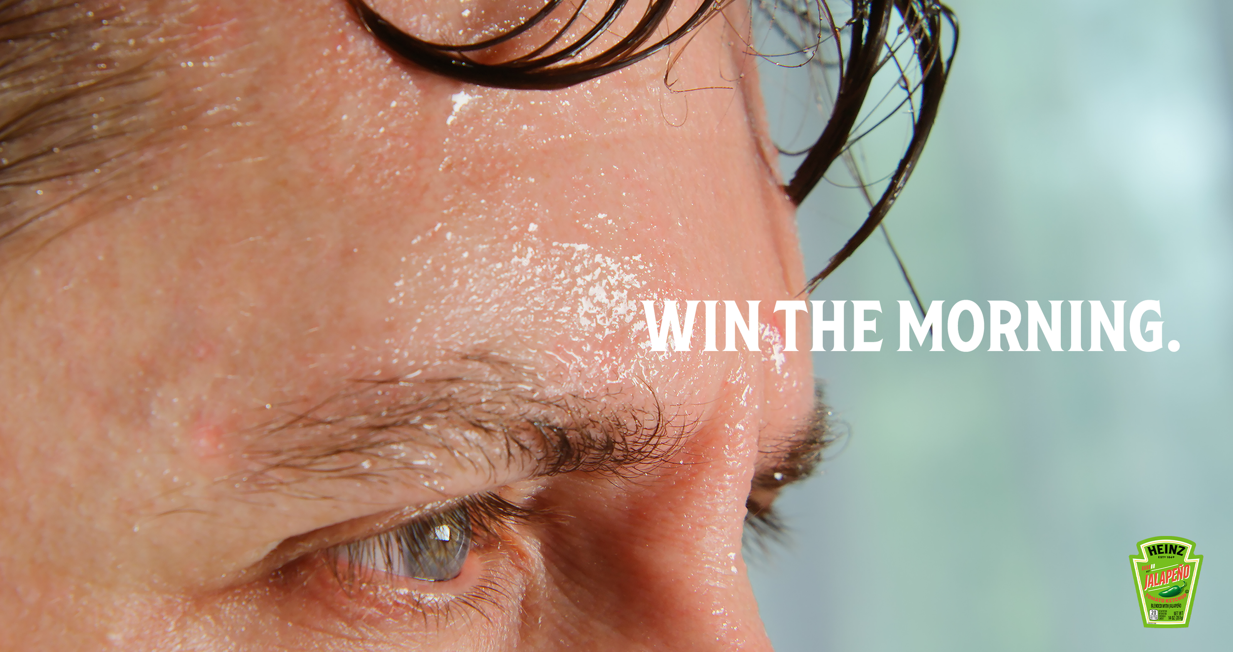 Speculative advertisement showing an extreme close-up of a person's sweaty forehead. White text reads "WIN THE MORNING." A small Heinz Jalapeno Ketchup logo is visible in the bottom right corner.
