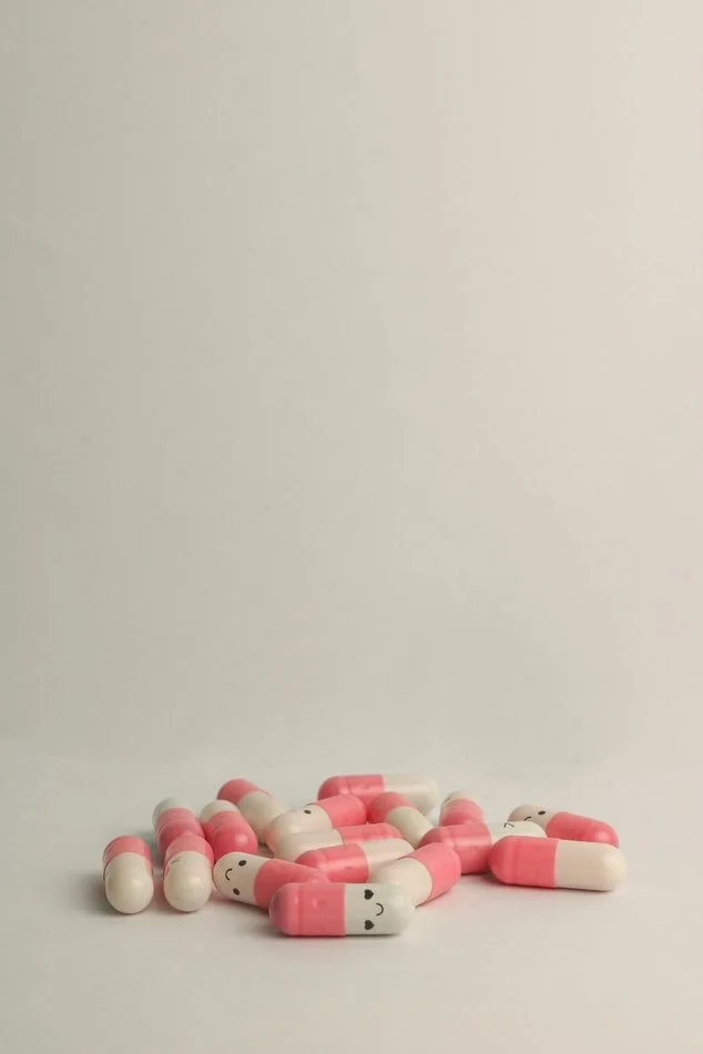 Close up of pink and white pills with smiley faces on them, resting on a white table.