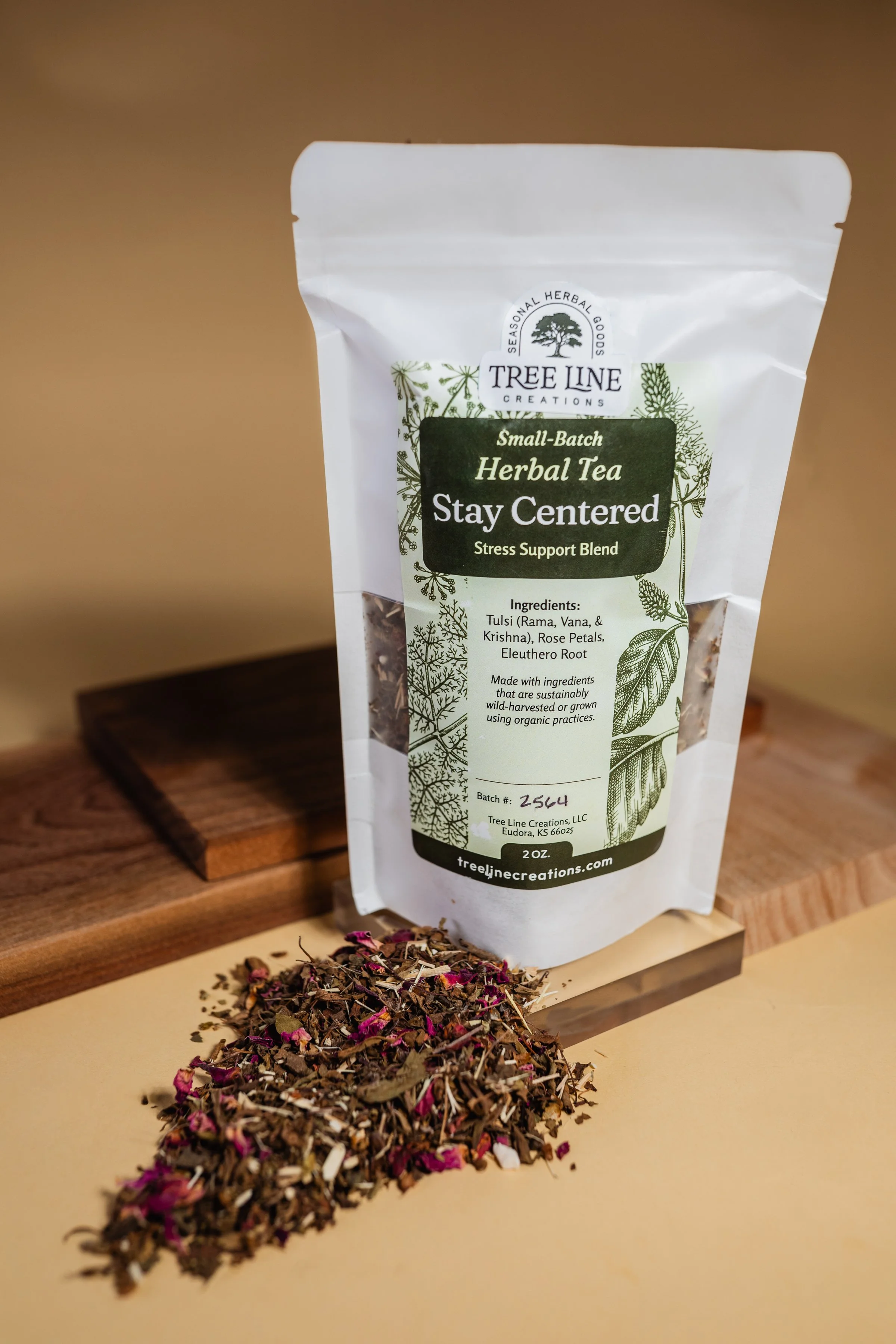 Wicker basket containing a bag of herbal tea labeled 'Keep Calm Tea', a copper teapot, a piece of mineral or crystal, and a gray cloth with frayed edges on a white surface.