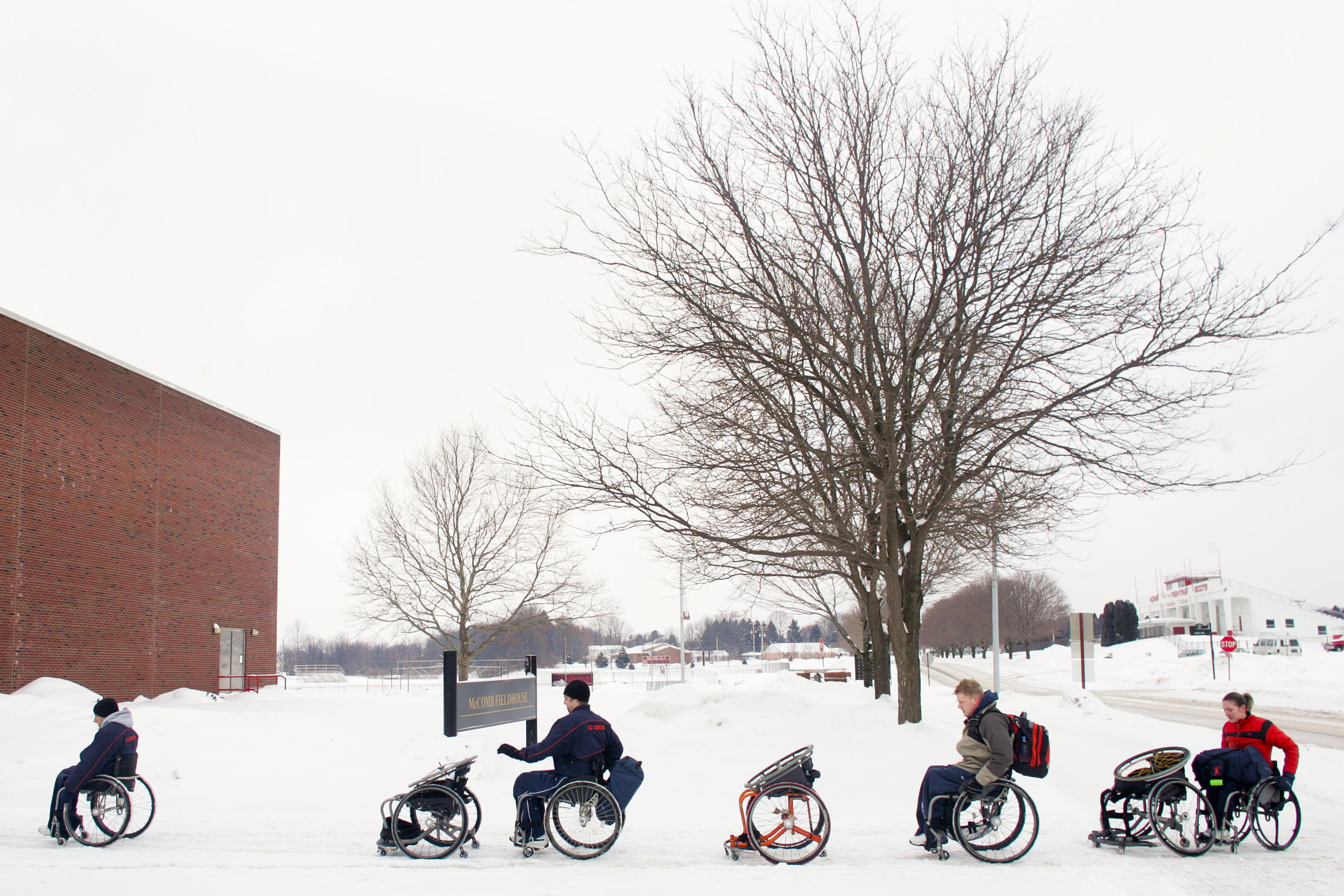 From left, Paul Ward, Brandon Wagner, Matt Buchi, and Edina Mueller push their game chairs through the snow on their way to a tournament at Edinboro University. Each athlete typically carries two chairs and spare wheels with them to every tournament. They don't have much traction with the uneven, snowy surface.