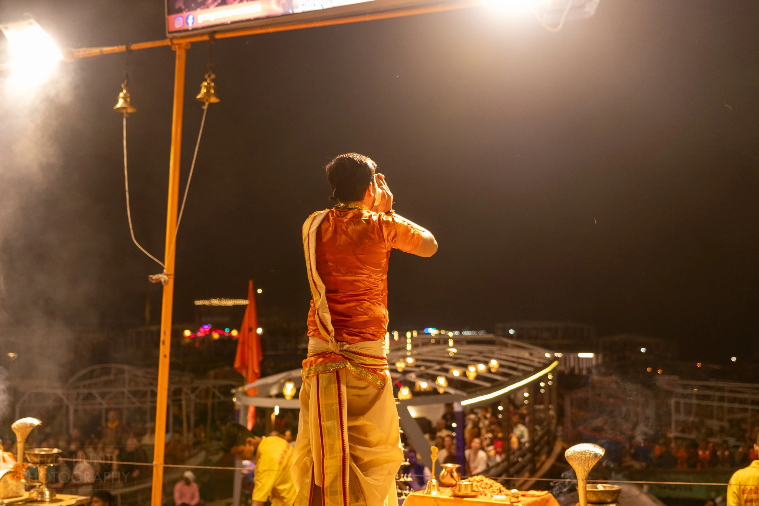 A man wearing an orange religious outfit conducts a religious ceremony called arti, Varanasi, India.