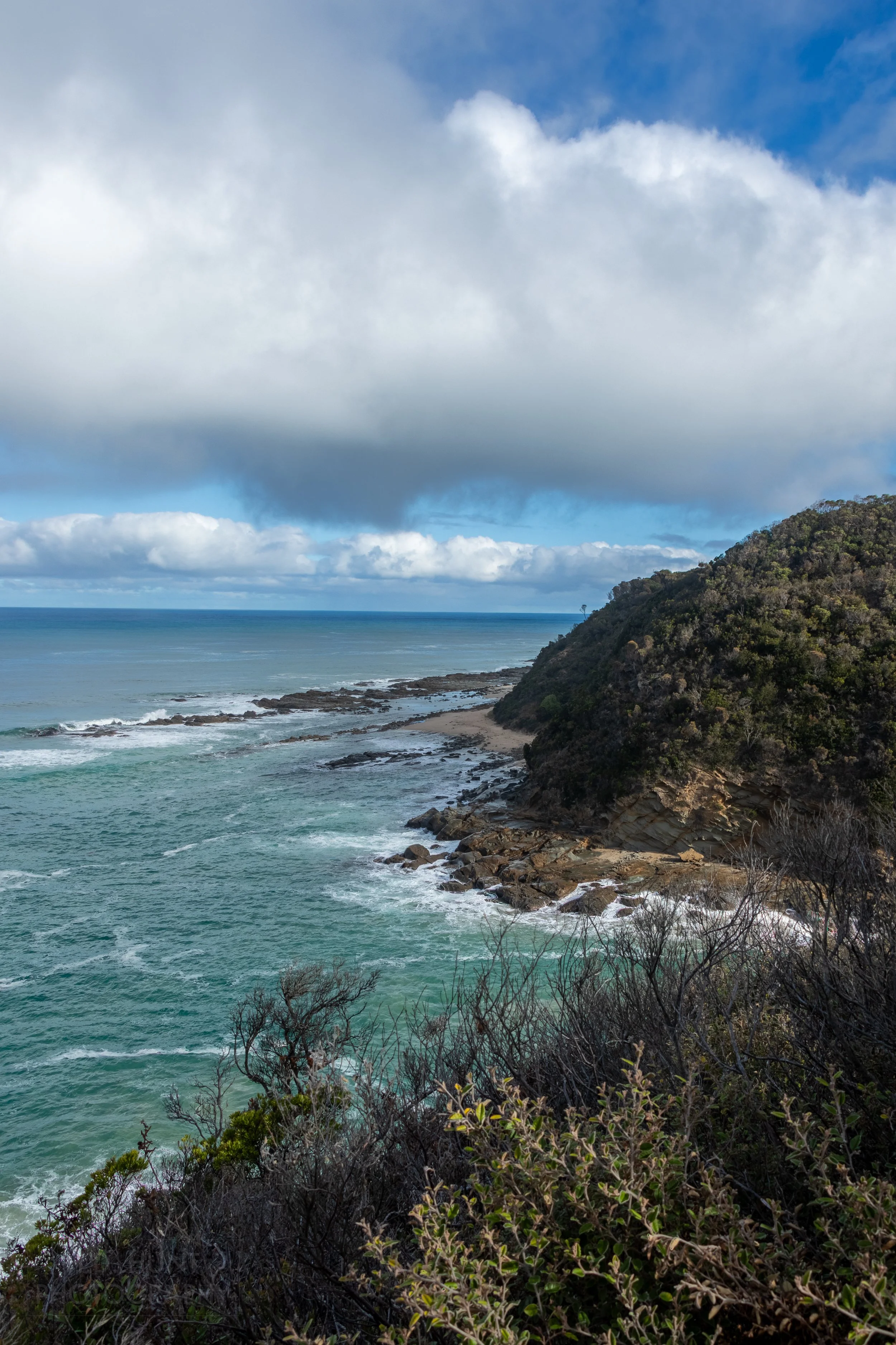 Waves meet a small beach and boulders beneath a cliff along The Great Ocean Walk, Victoria, Australia.