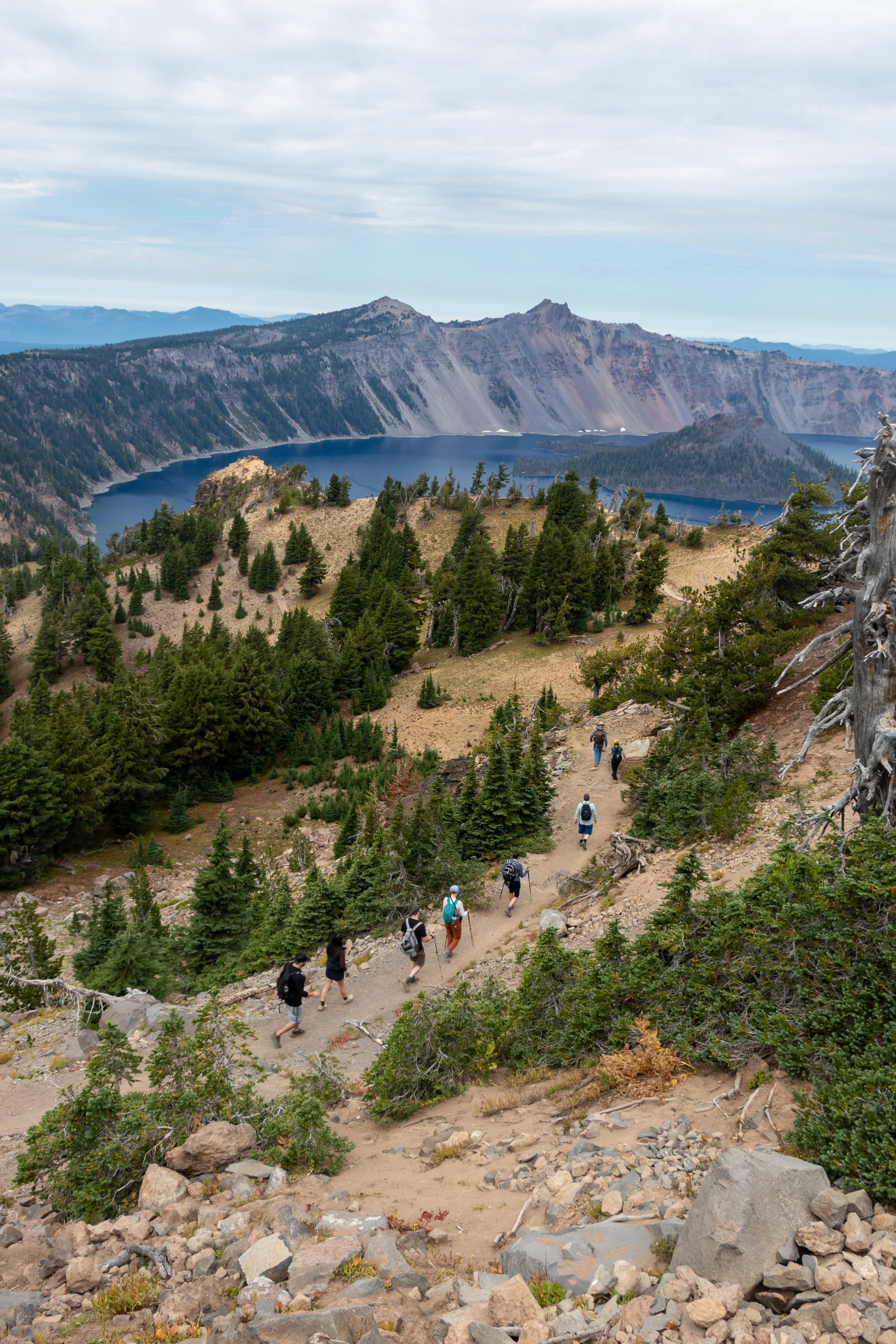 Hikers walk along a trail with Crater Lake and Wizard Island in the background, Crater Lake National Park, Oregon, United States.