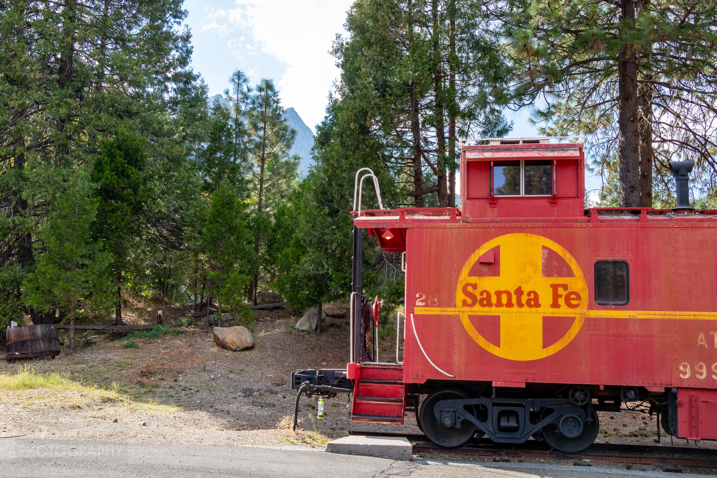 A red and yellow Santa Fe railroad caboose is seen in the foreground with tall pine trees and mountains in the background, Jubilee Railroad Wilderness Lodge, Dunsmuir, California, United States.