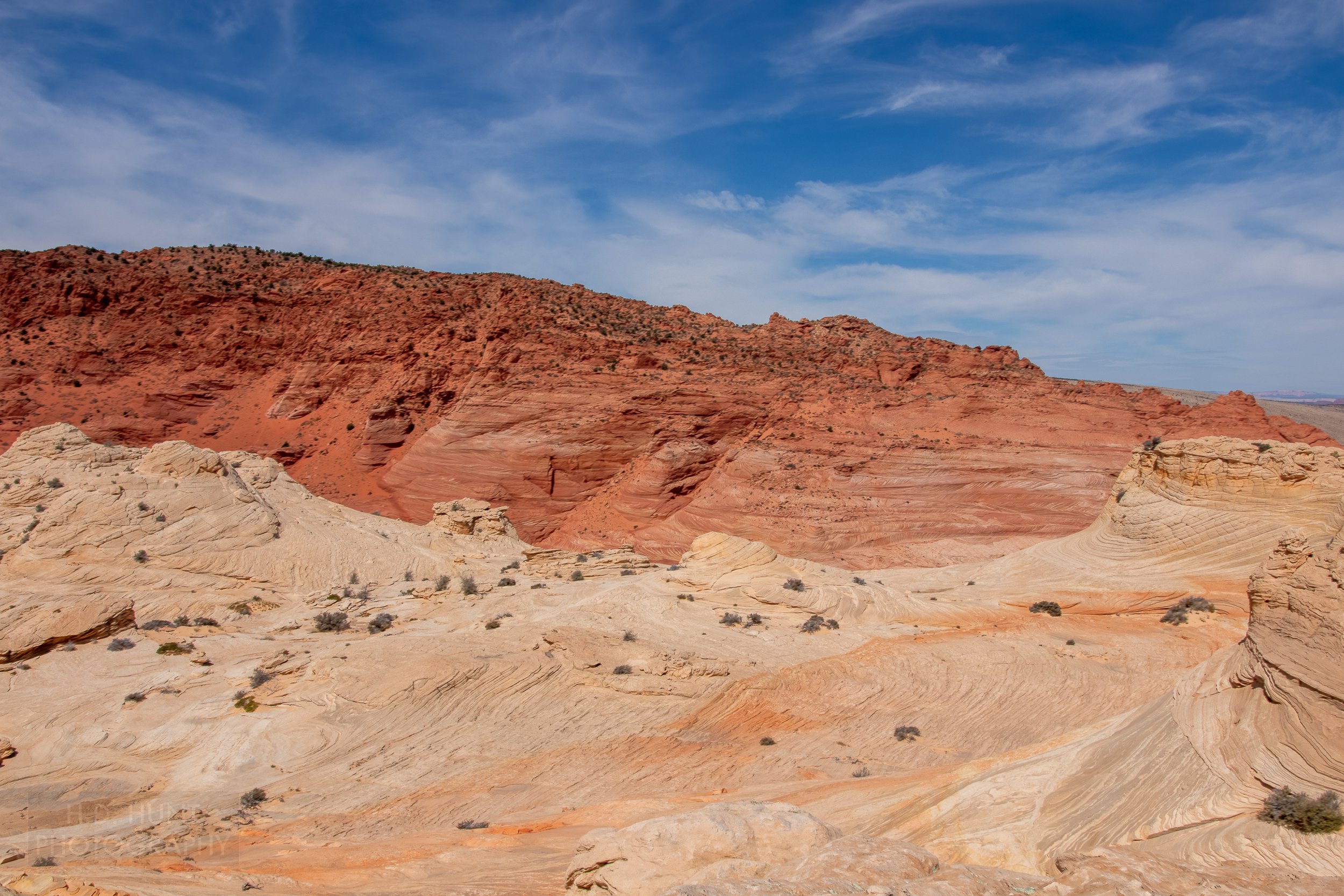 Heavily deformed white sandstone is seen in the foreground of a large cliff of striped red sandstone in Coyote Buttes North, Paria Canyon-Vermilion Cliffs Wilderness, Arizona, United States.