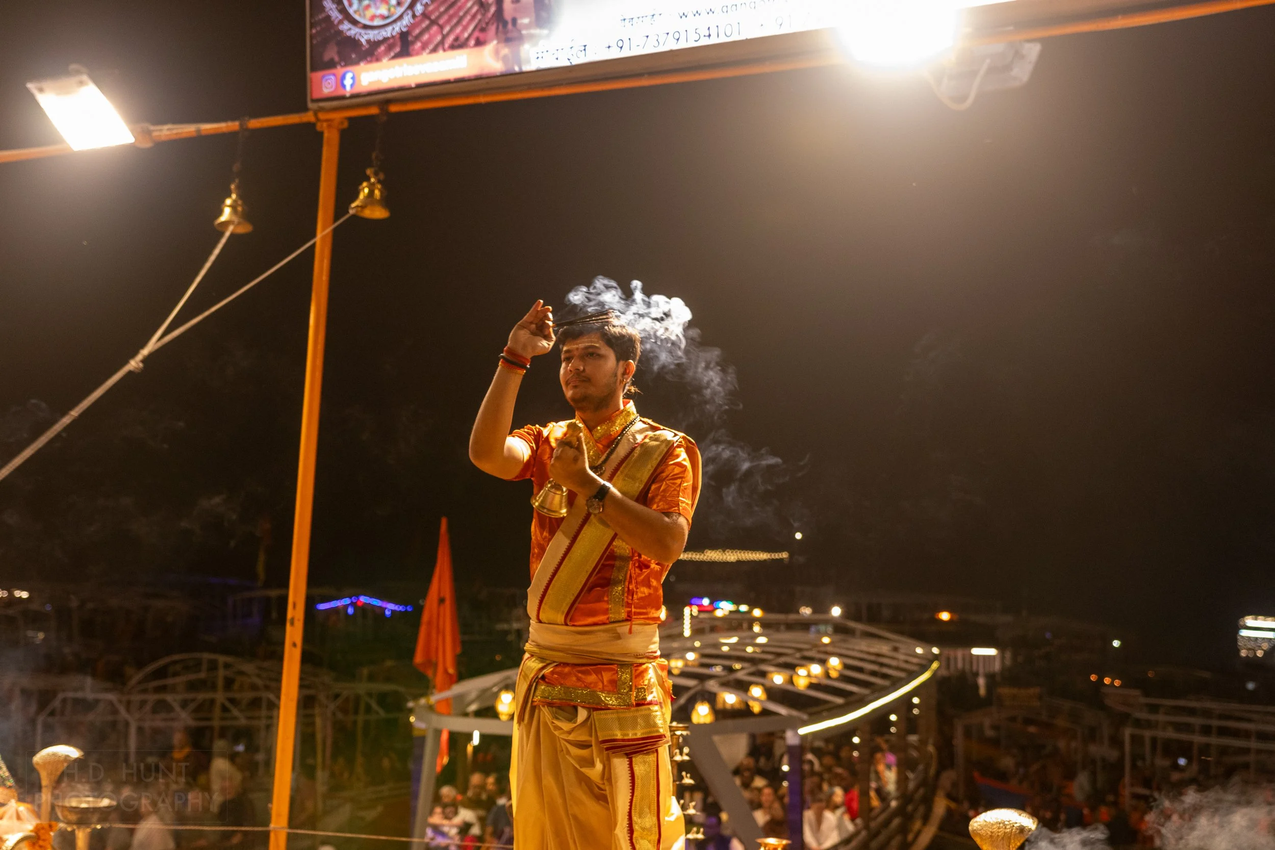 A man wearing an orange religious outfit waves incense during a Hindu religious ceremony called arti, Varanasi, India.